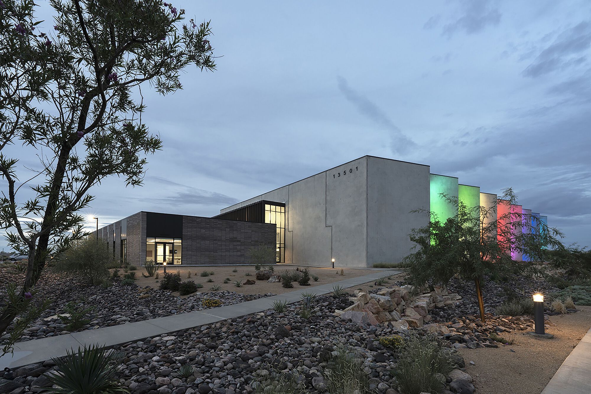 Concrete and brick volumes with illuminated vertical fins and desert landscaping at dusk