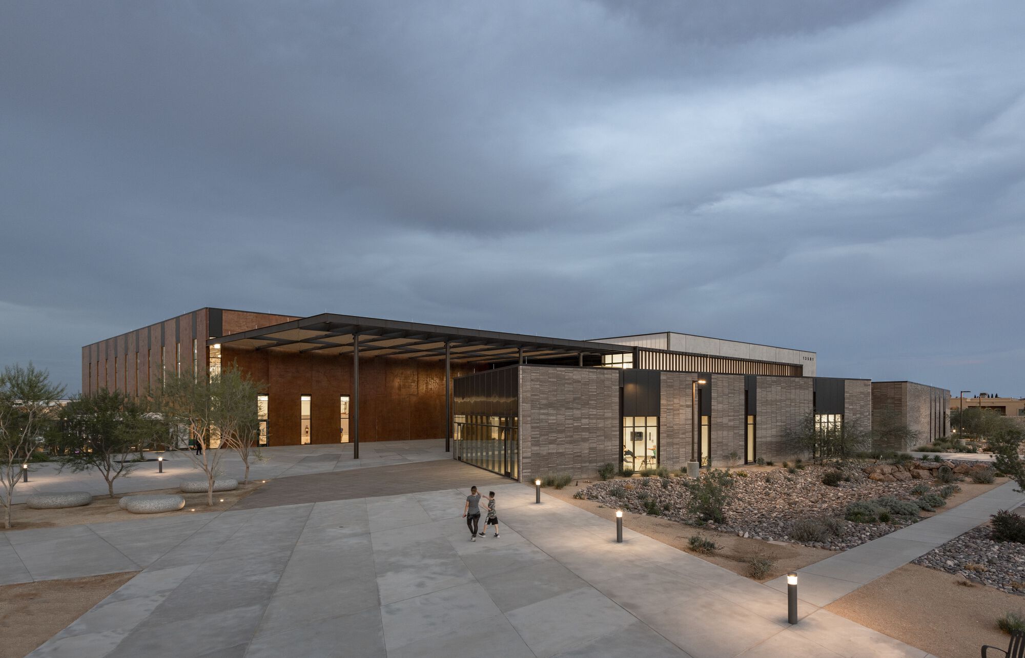 Entry plaza with vertical timber screen and canopy under overcast skies at twilight