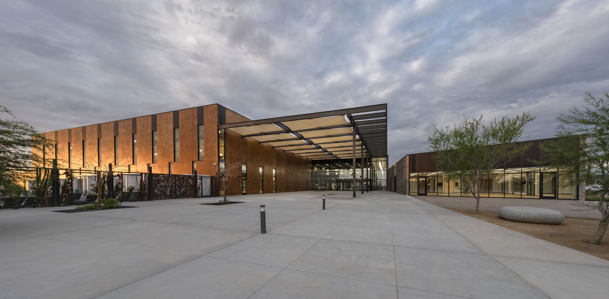 Glass entry pavilion with projecting canopy flanked by timber screen walls at dusk