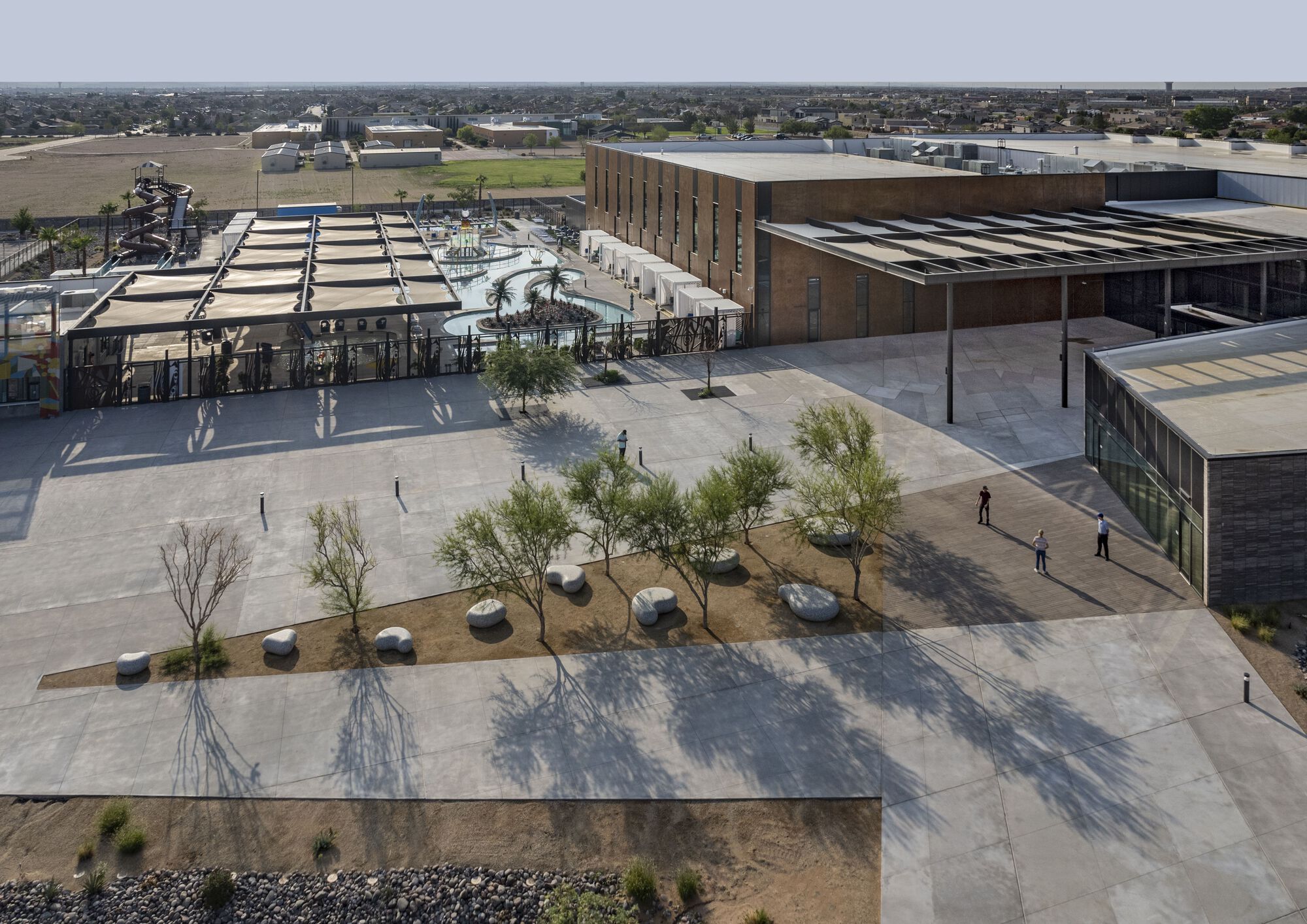 Aerial view of plaza with scattered boulders and young trees casting shadows on pavement