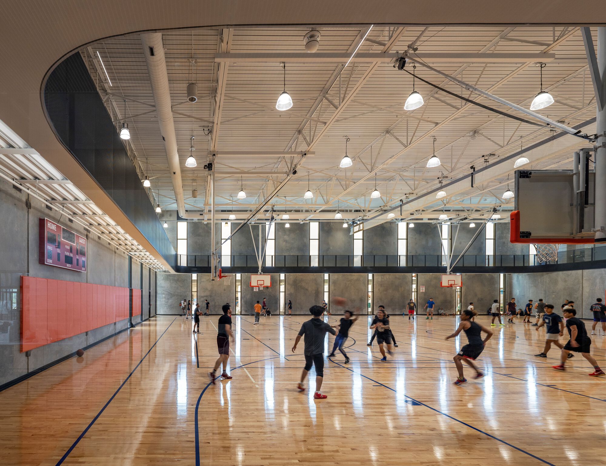 Indoor basketball court with wood floor, exposed steel trusses and players in motion