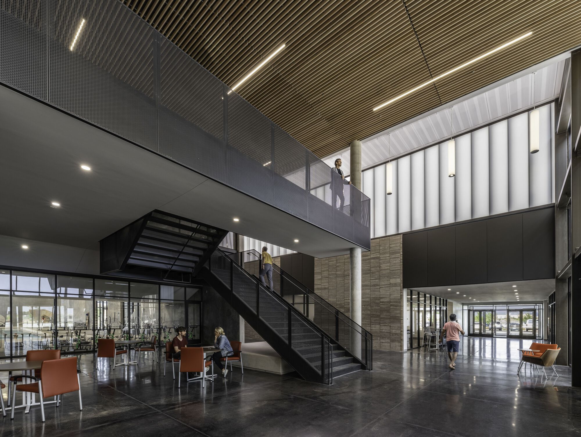 Double-height lobby with black steel staircase, slatted wood ceiling and visitors below