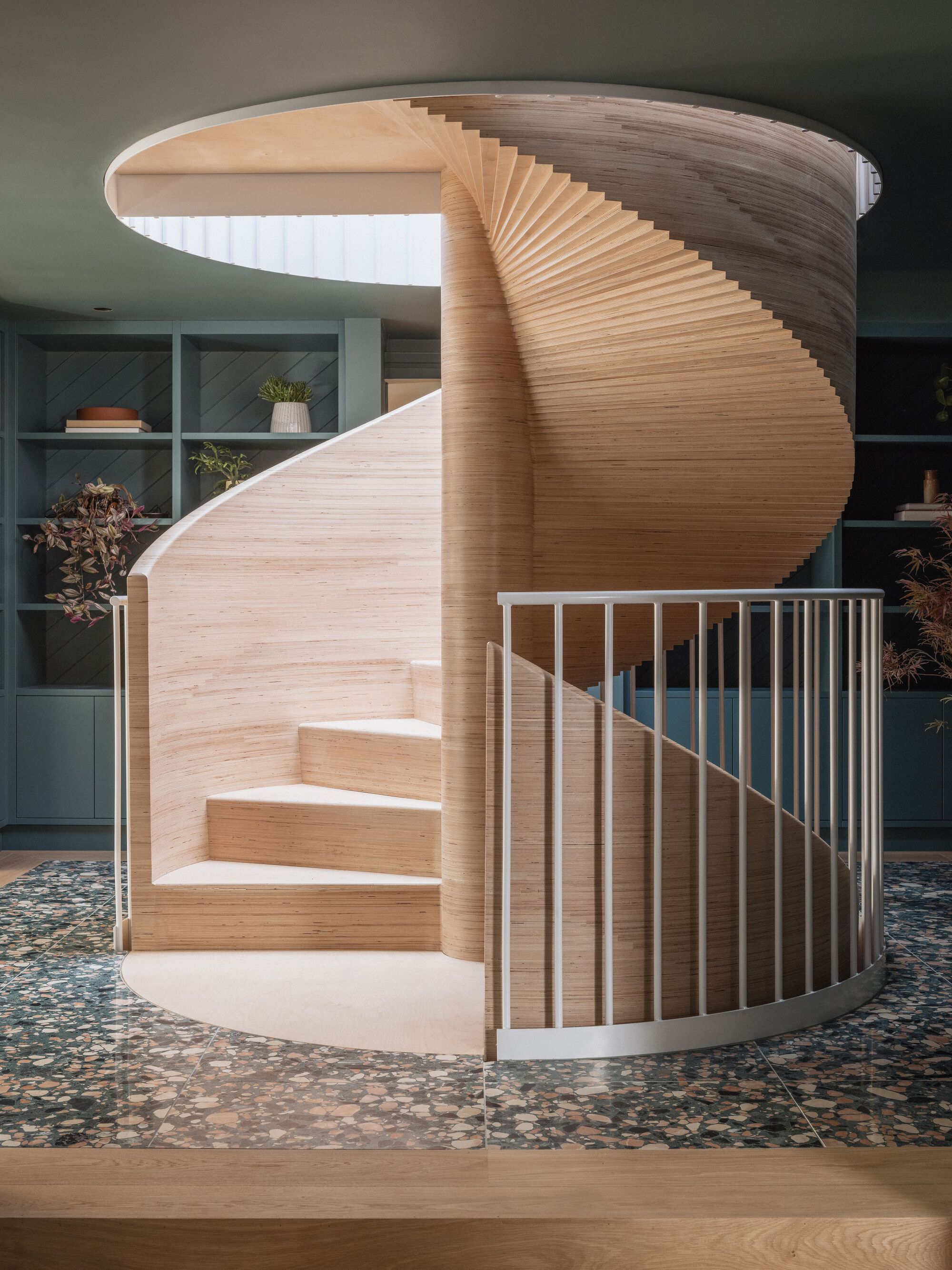 Helical timber staircase with horizontal slat detail and white metal balustrade over terrazzo flooring