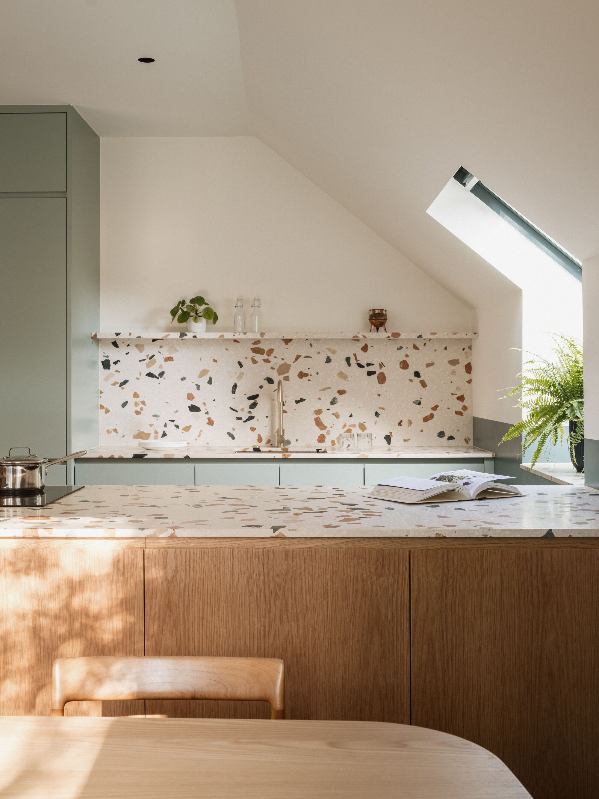 Kitchen island with terrazzo countertop and backsplash beneath an angled skylight in morning light