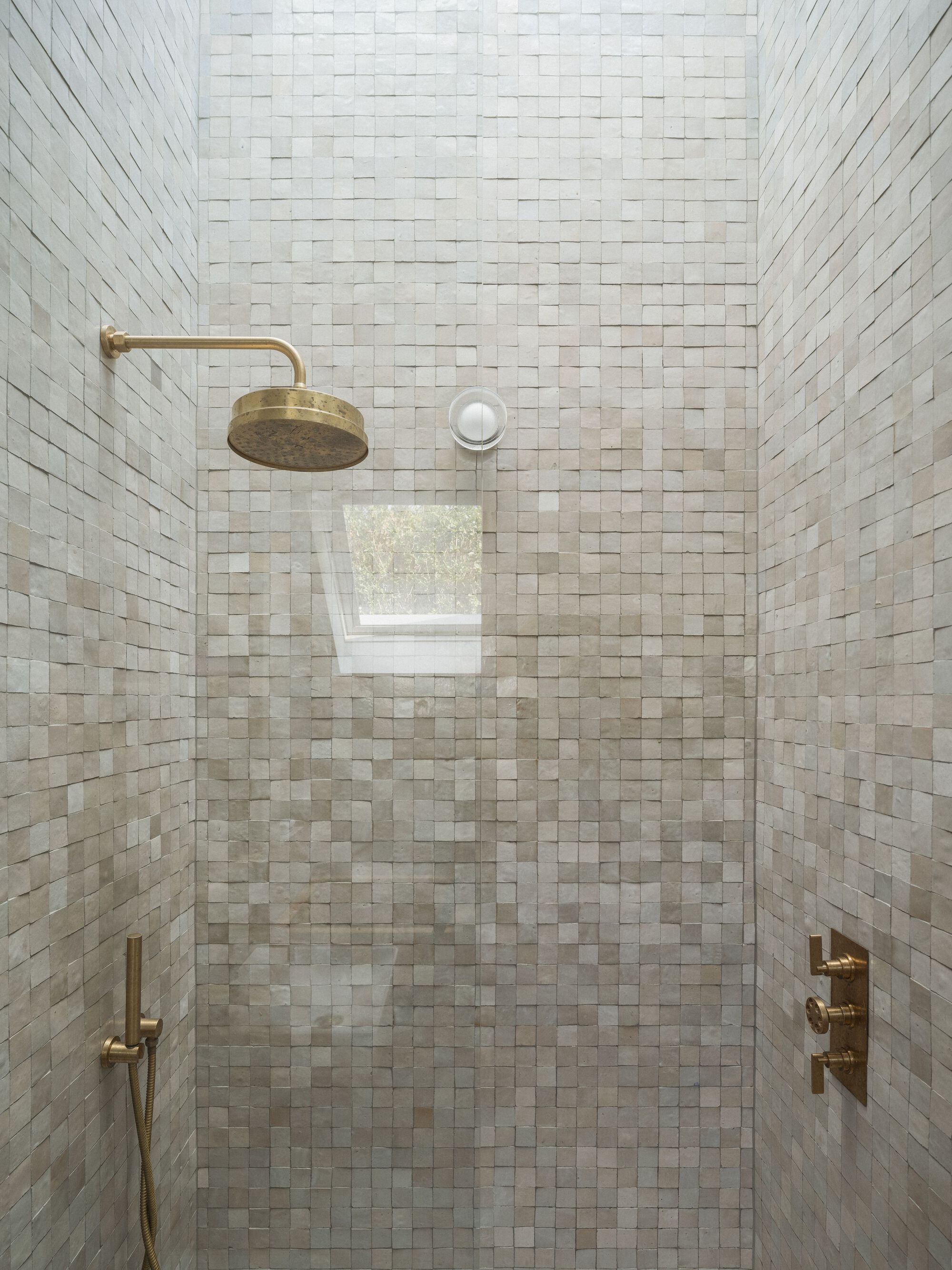 Shower enclosure lined with small white mosaic tiles and brass fixtures