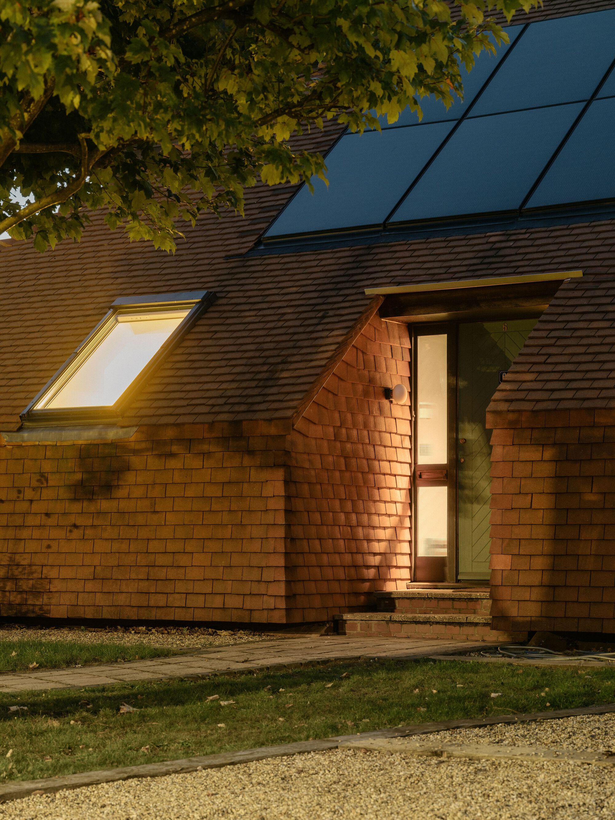 Exterior facade clad in cedar shingles with illuminated skylight and doorway visible at dusk