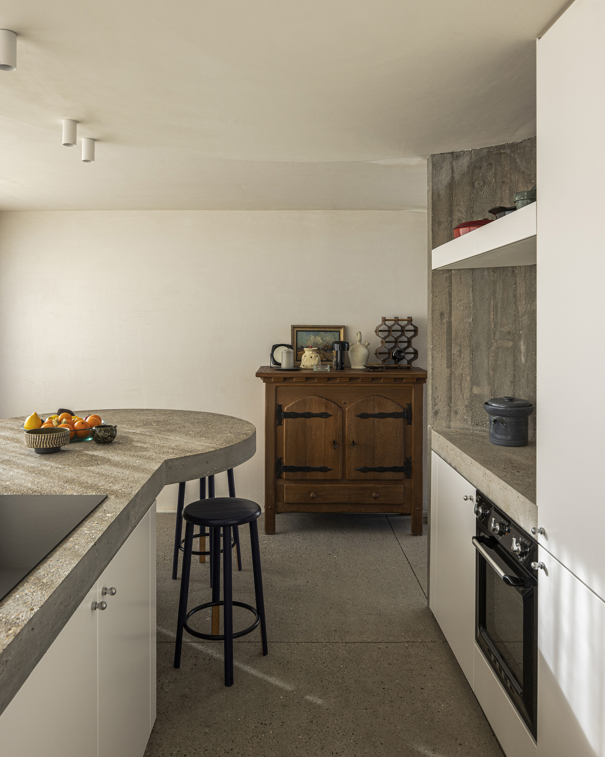 Kitchen with curved concrete island, terrazzo floor, and board-formed concrete wall in natural light