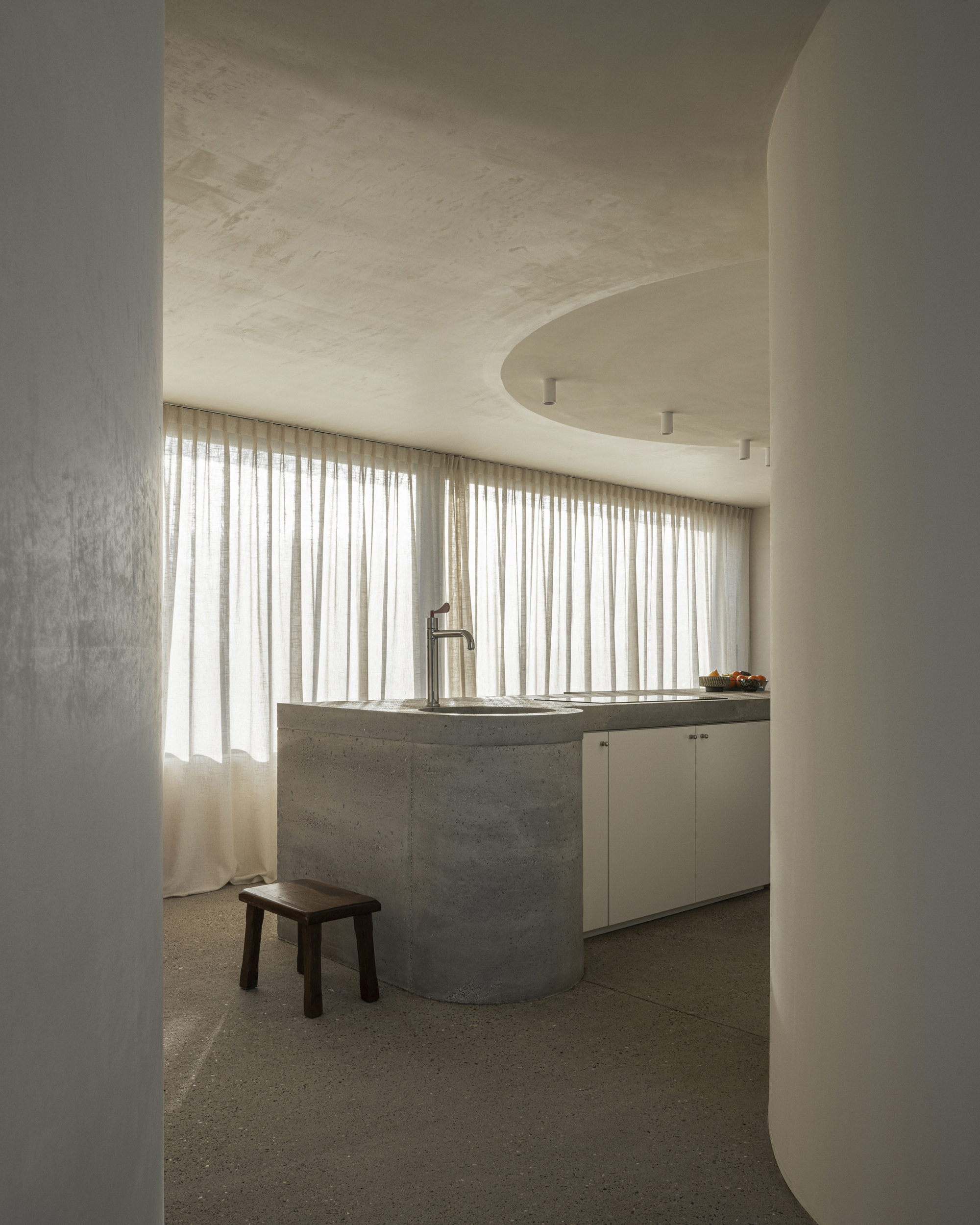 Arched doorway framing kitchen counter with board-formed concrete base and full-height curtained window