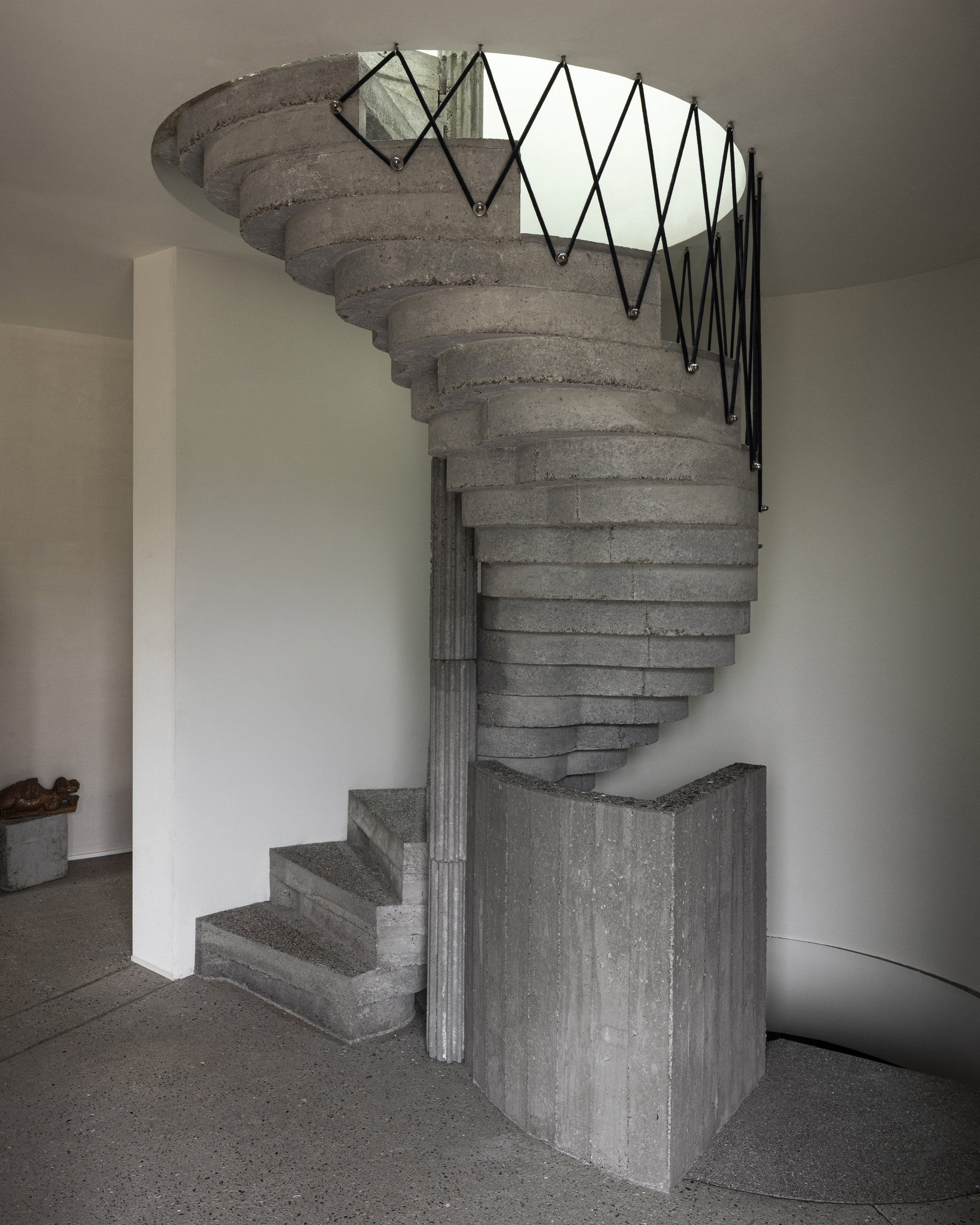 Helical concrete stair with zigzag metal railing and board-formed central column rising through circular opening