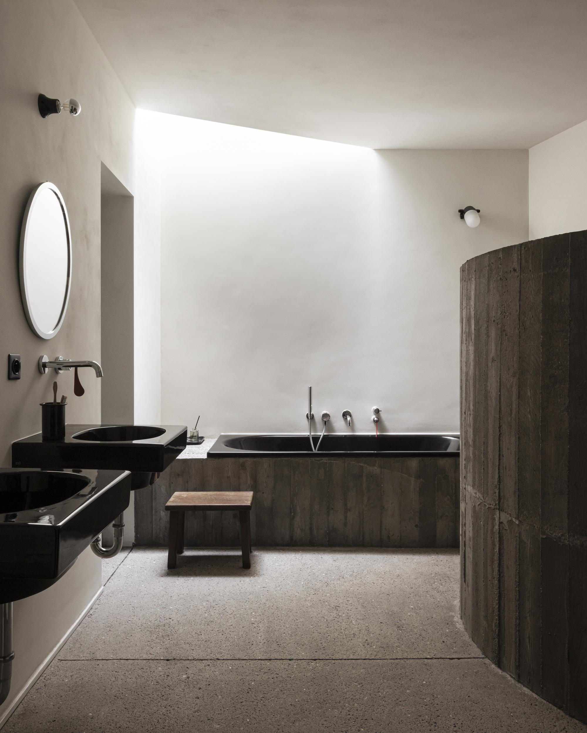Bathroom with black vessel sinks, board-formed tub surround, and skylight washing white plaster walls