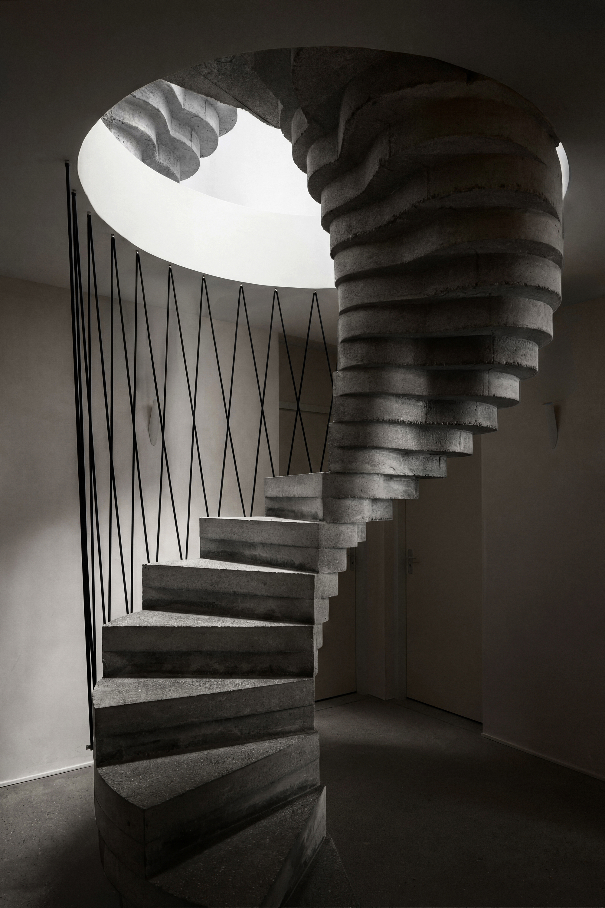 View up the spiral concrete staircase with zigzag steel balustrade beneath a circular skylight