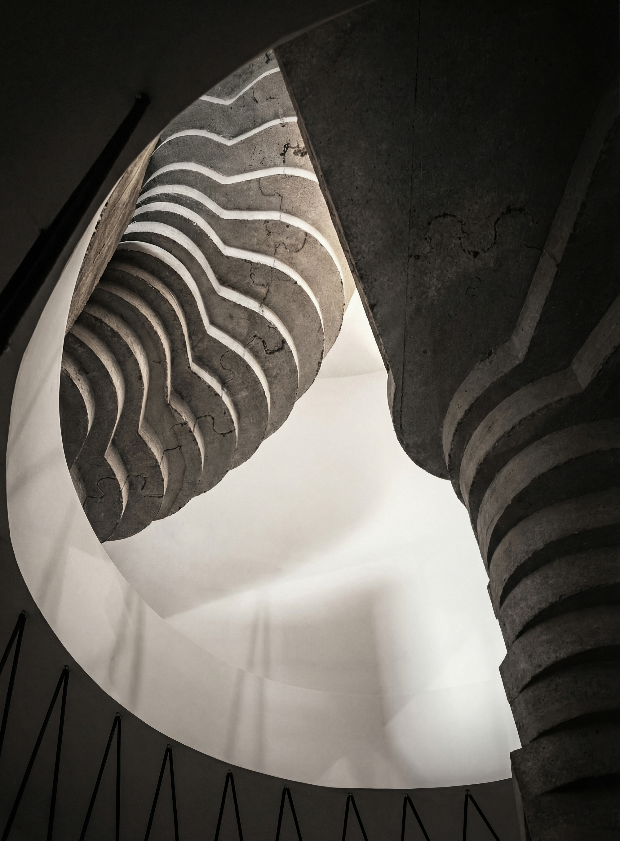 Looking up at the spiraling concrete staircase with wavy formwork patterns under natural light