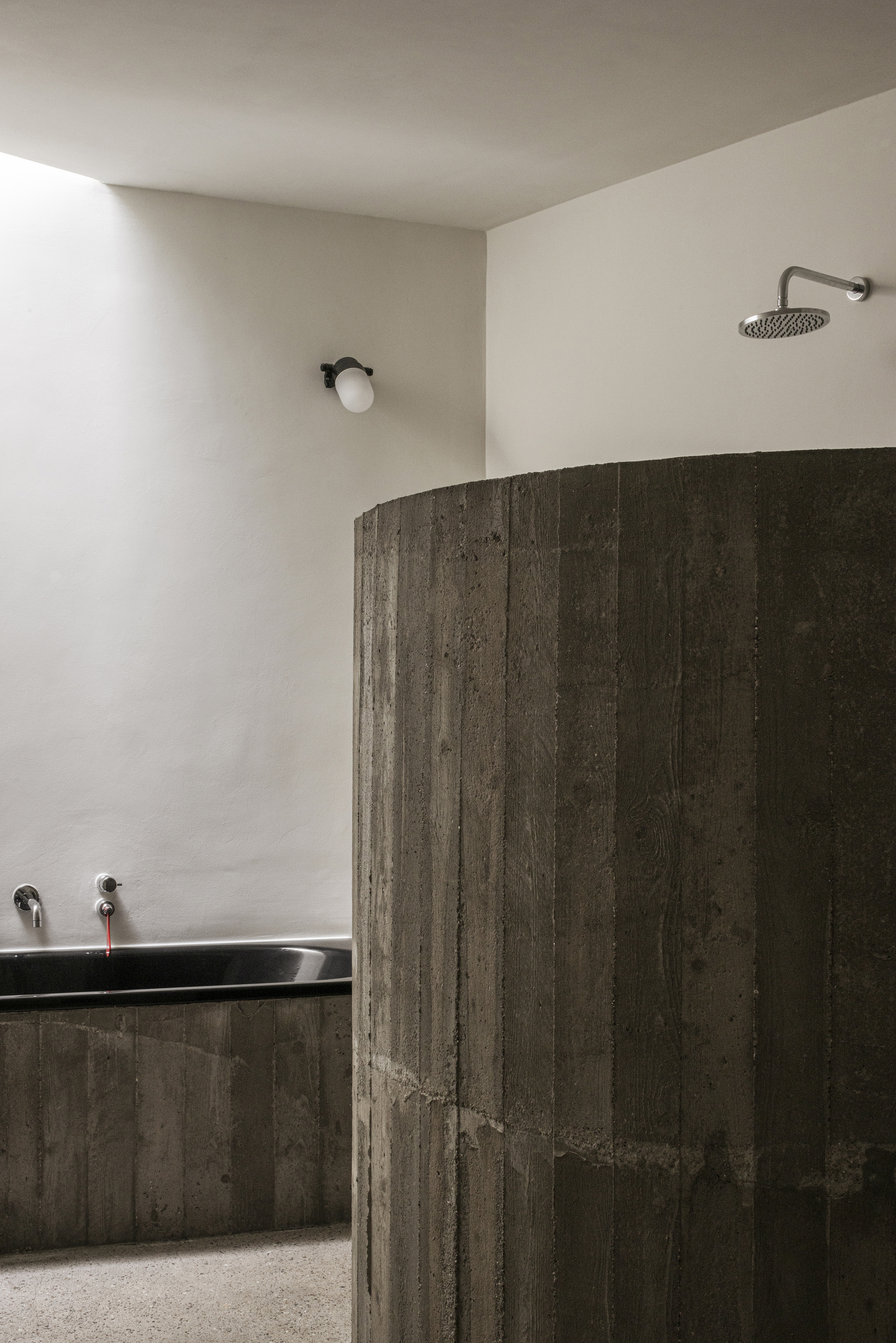 Curved board-formed concrete shower wall with wall-mounted rainfall showerhead and minimal fixtures