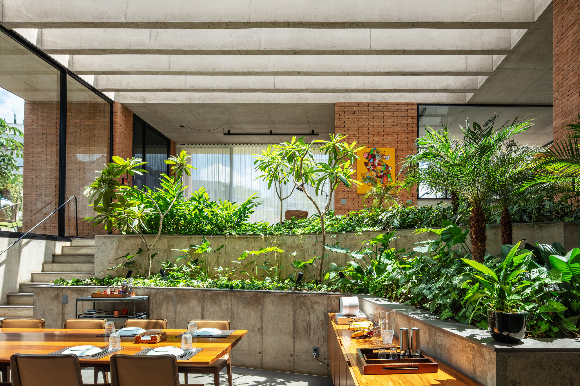 Dining area with timber table facing tiered concrete planters filled with foliage beneath skylight