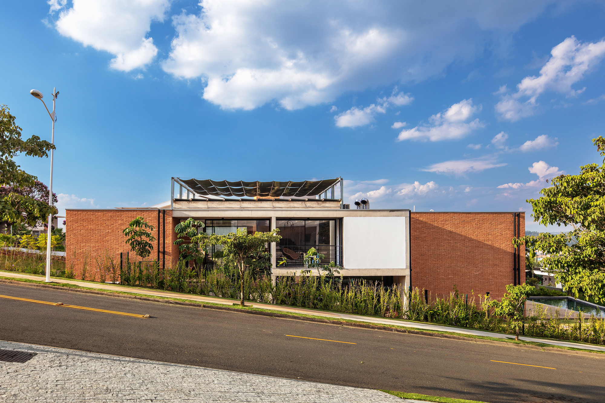 Facade composition with brick volumes, white panel, planted verge and exposed roof structure under blue sky