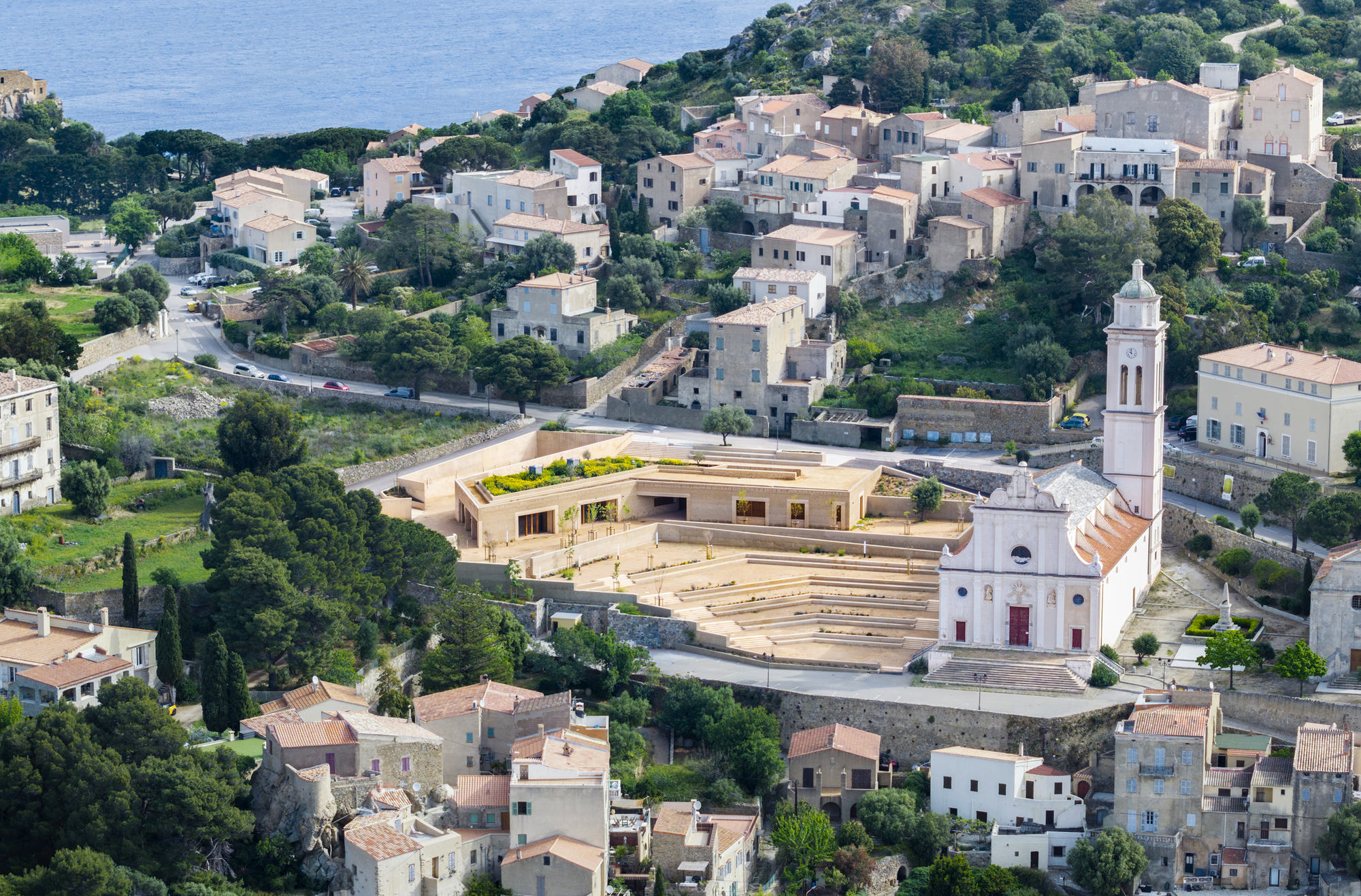 Aerial view of the terraced amphitheater and low-slung volumes nestled among hillside houses and a white church tower