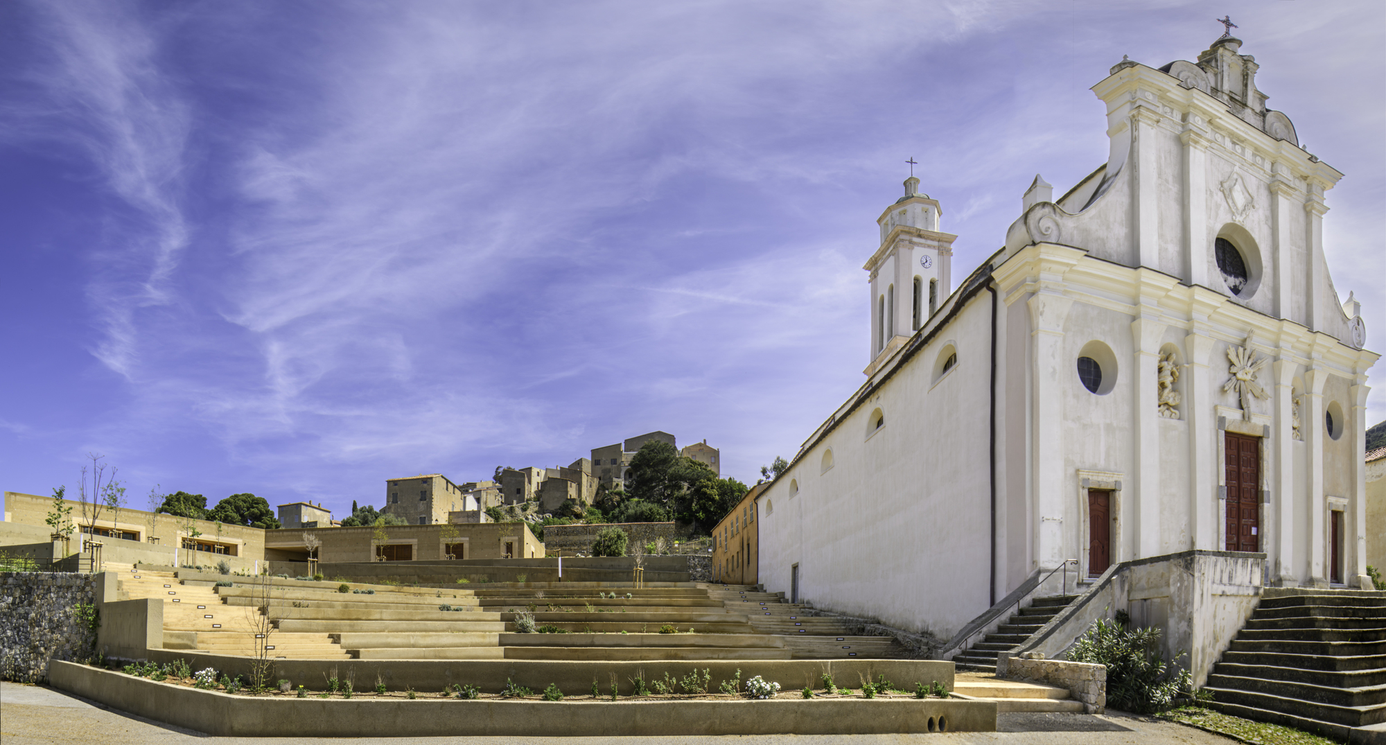Wide concrete stepped terraces rising from the white church facade toward the village on the slope beyond