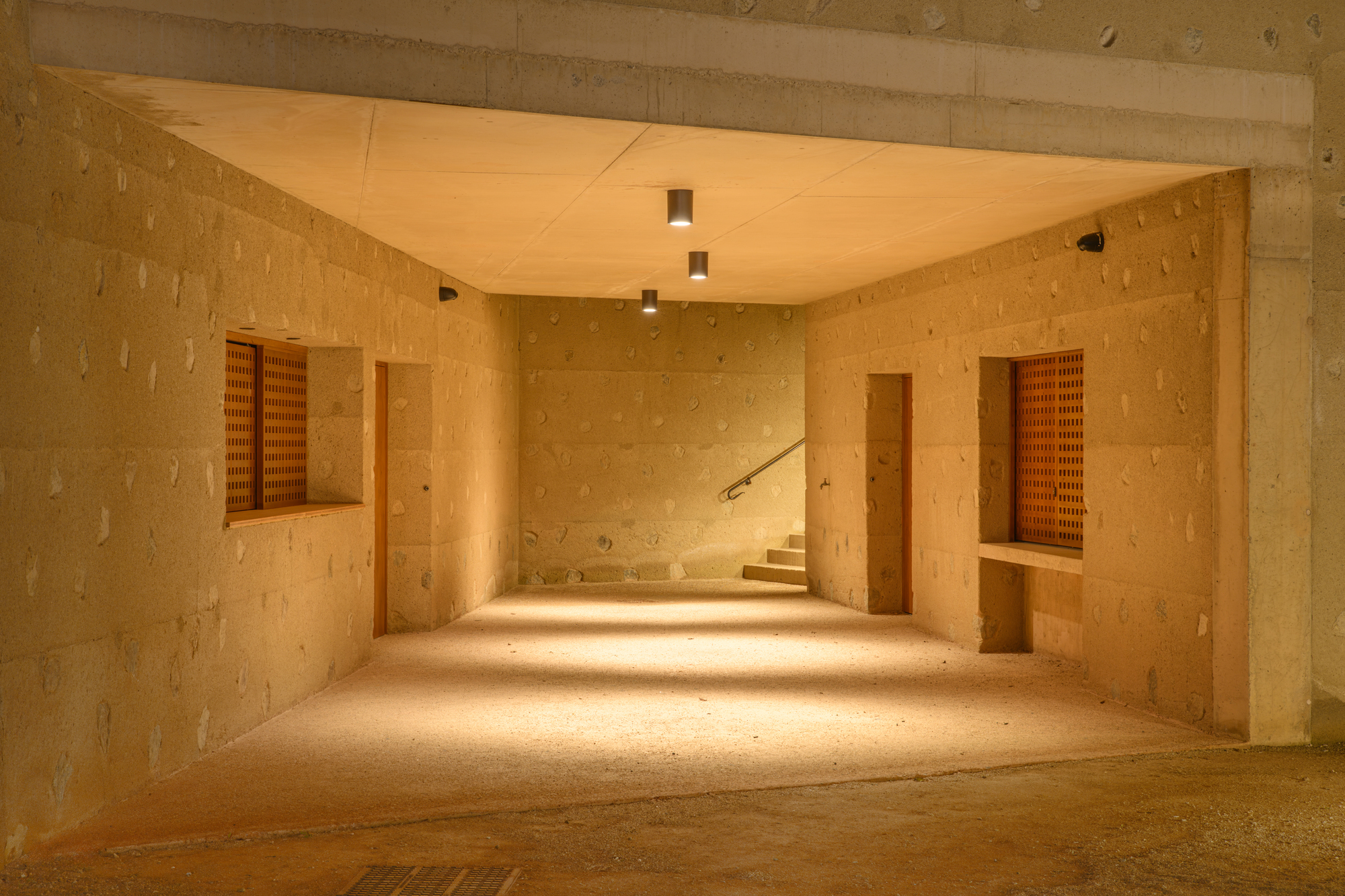 Interior corridor with rammed earth walls, wood shutters and warm light spilling across the floor at dusk
