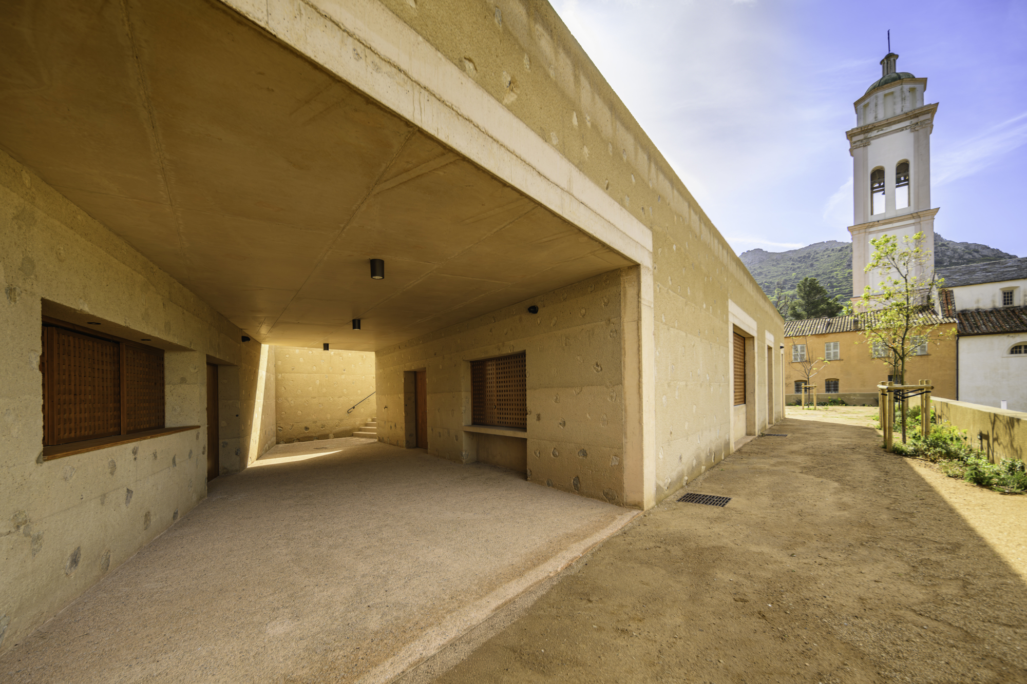 Covered entry passage with exposed concrete soffit and church bell tower visible beyond