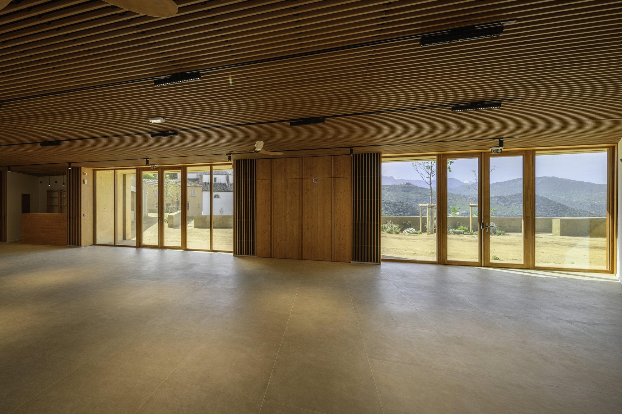 Interior hall with slatted timber ceiling and floor-to-ceiling windows framing distant mountain views