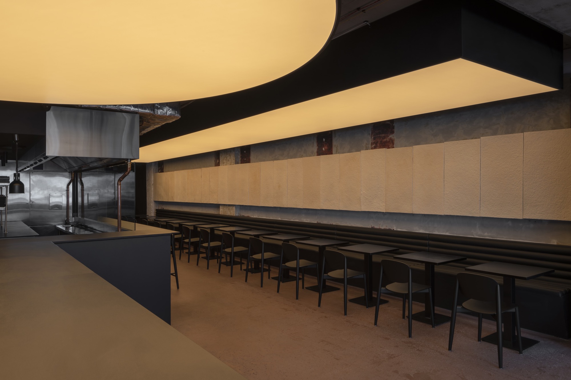 Interior dining space with curved luminous ceiling panels above a long communal table and black chairs