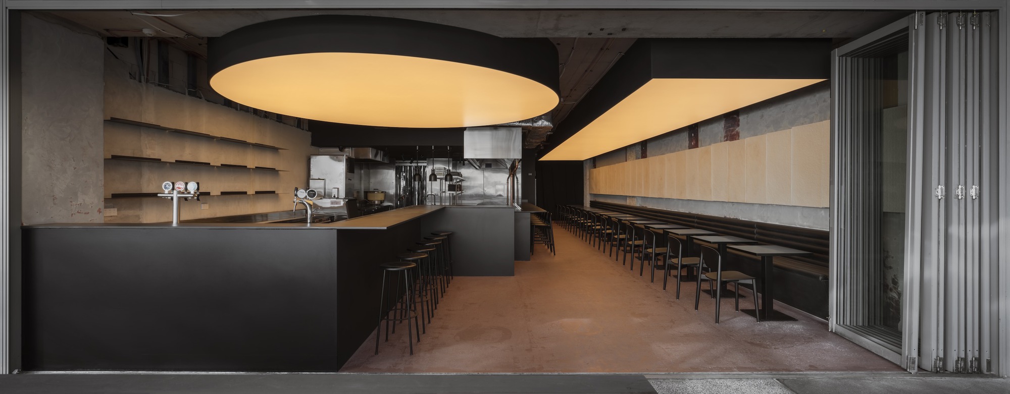 Wide view of the bar and dining area showing exposed concrete ceiling and open display shelving