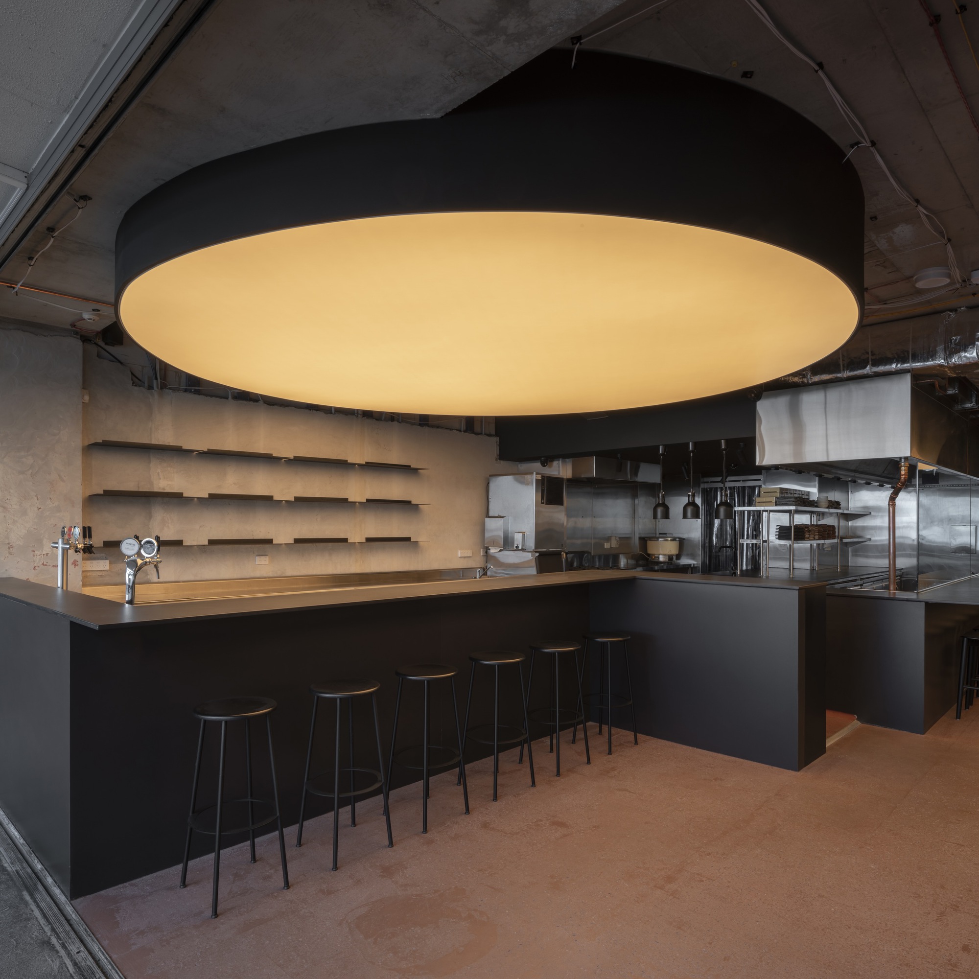 Central bar counter with black metal stools beneath a large circular light fixture