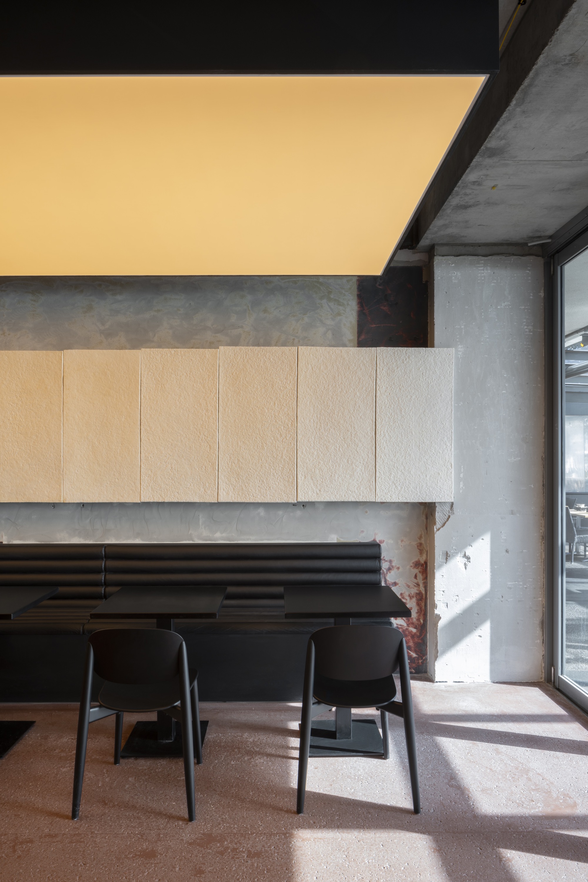 Window-side seating nook with wooden wall panels and sunlight falling across concrete floor