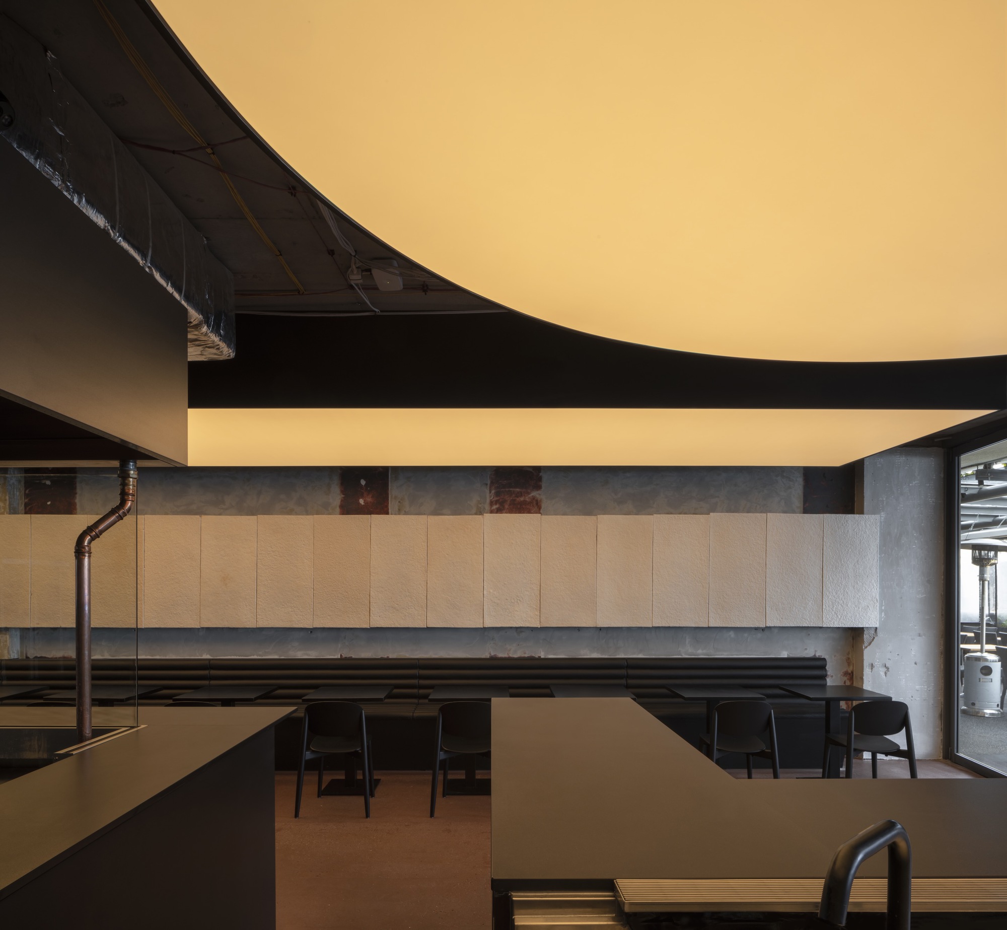 Dining area with wood panel wall and exposed black piping below a curved ceiling element