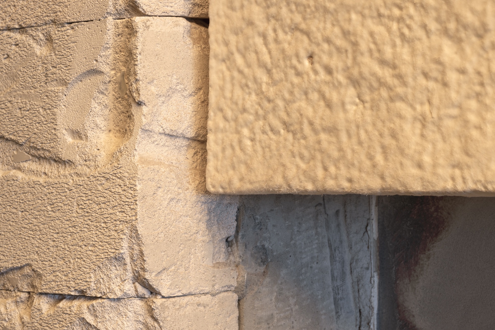Close-up of stone and concrete junction with textured cream panel in warm sunlight