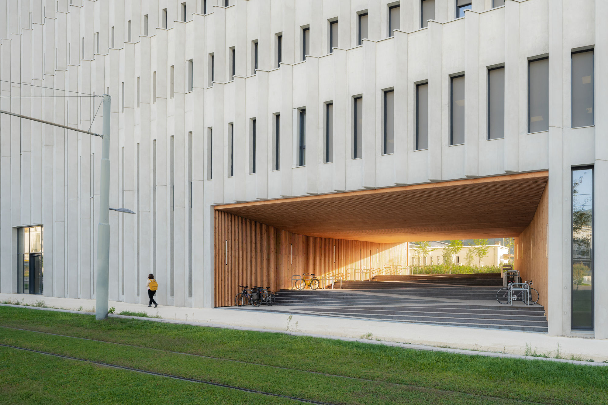Timber-clad entrance canopy recessed beneath the white slatted facade with a person walking by