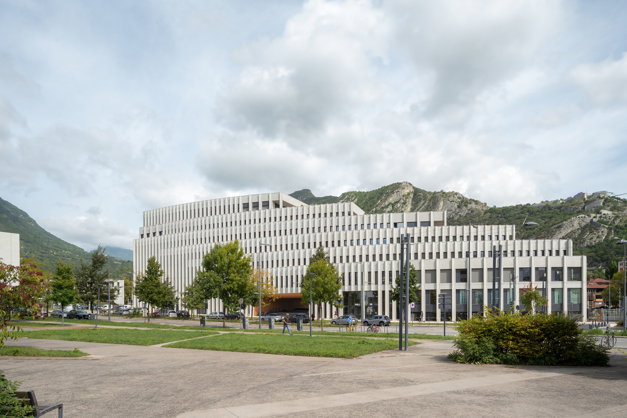 View across the park lawn showing the terraced facade stepping down against the mountains