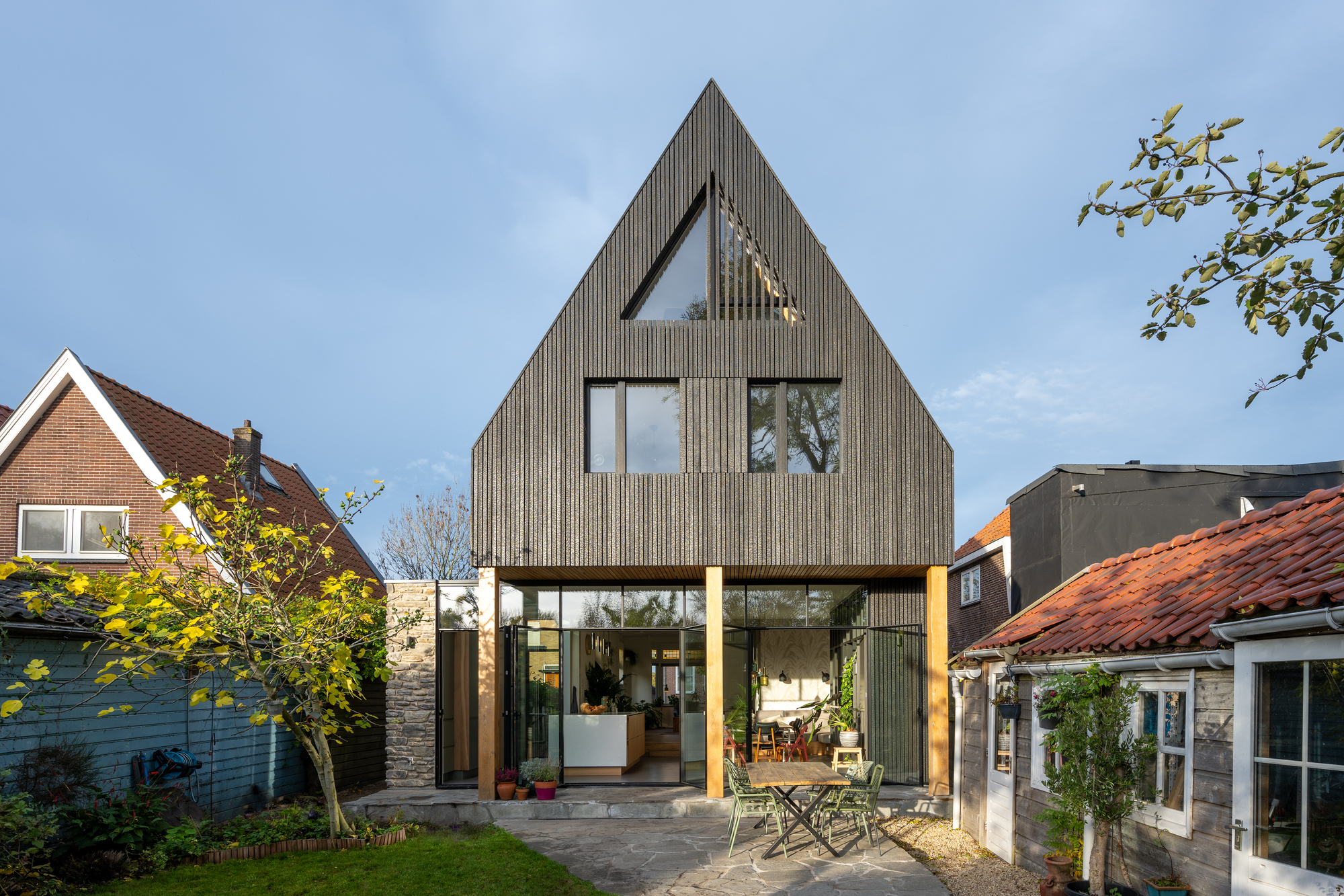 Rear garden view of the steeply pitched gable with vertical cladding and timber-framed canopy