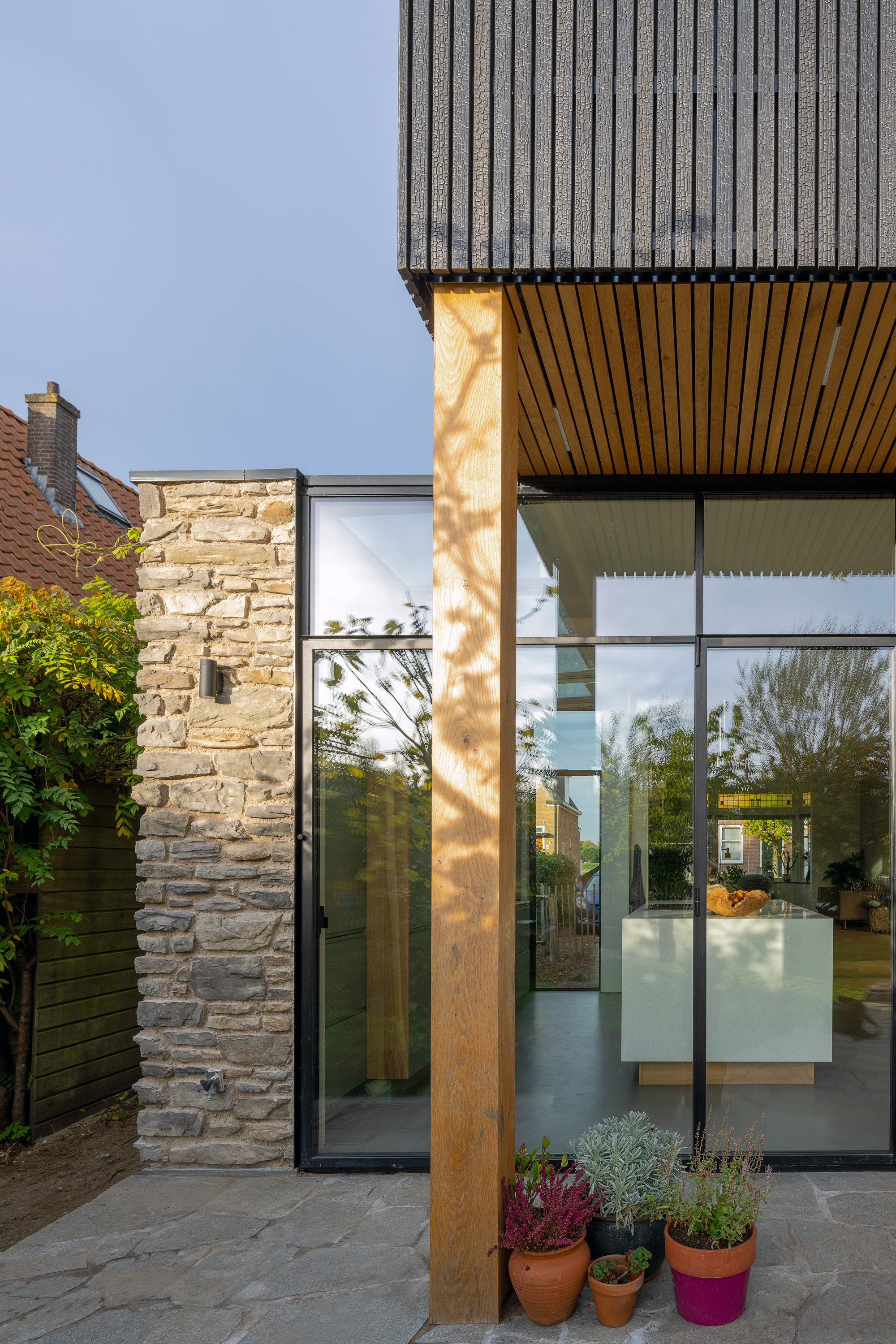 Glazed corner entry with timber column catching afternoon sunlight and potted plants below