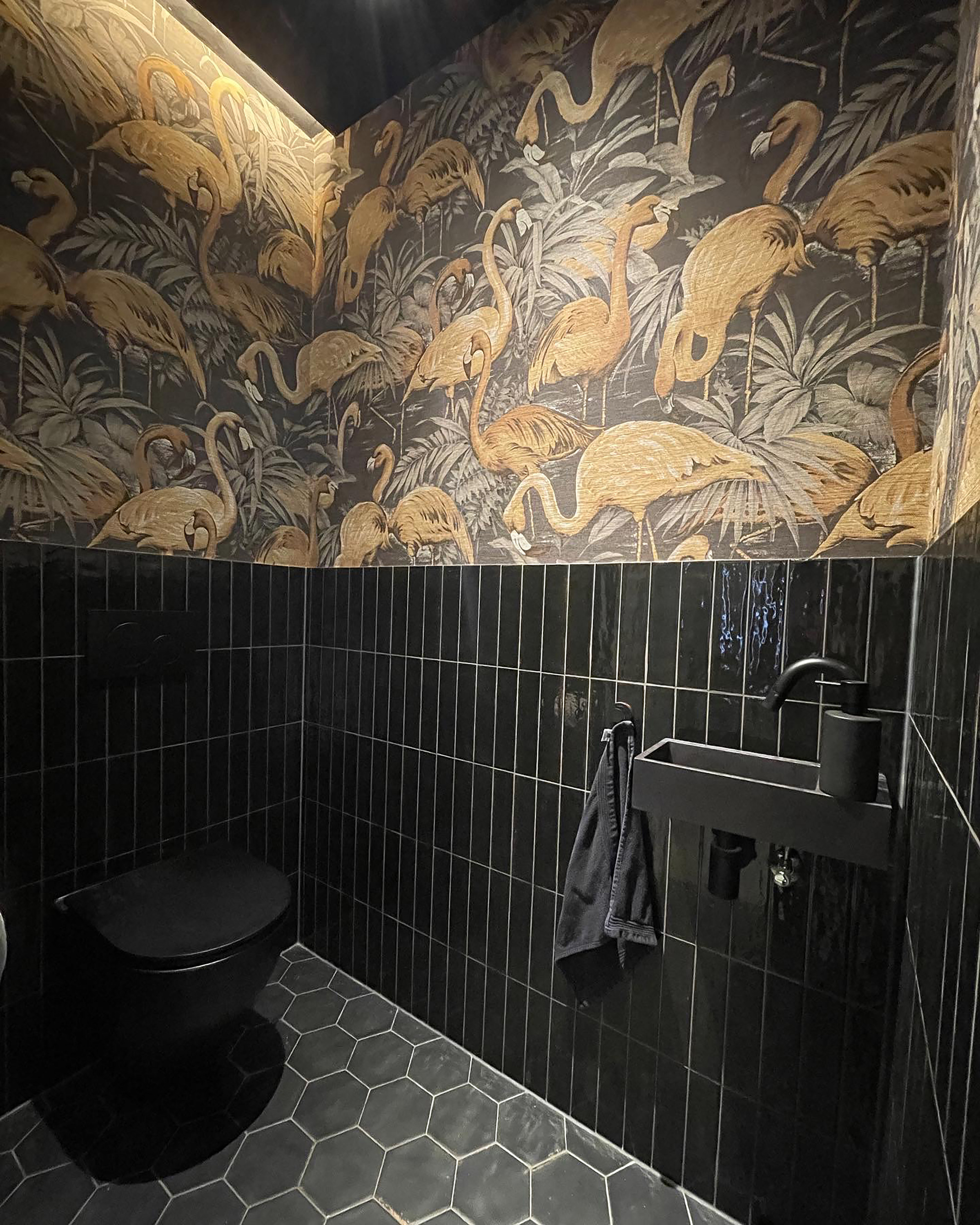 Powder room with black vertical tile wainscoting beneath a gold flamingo-patterned wallpaper mural