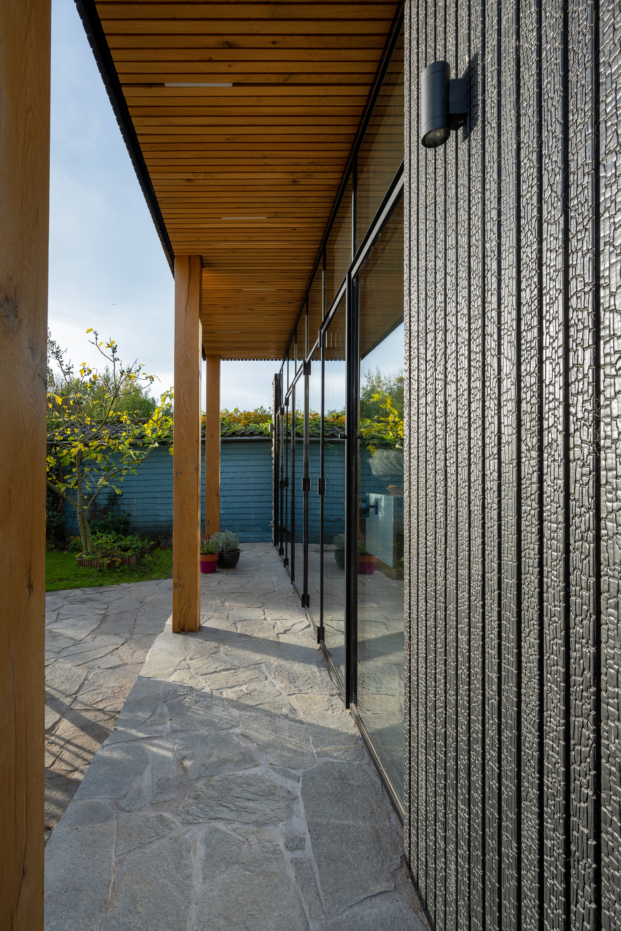 Covered terrace with timber posts and ceiling alongside textured brick wall and floor-to-ceiling glazing