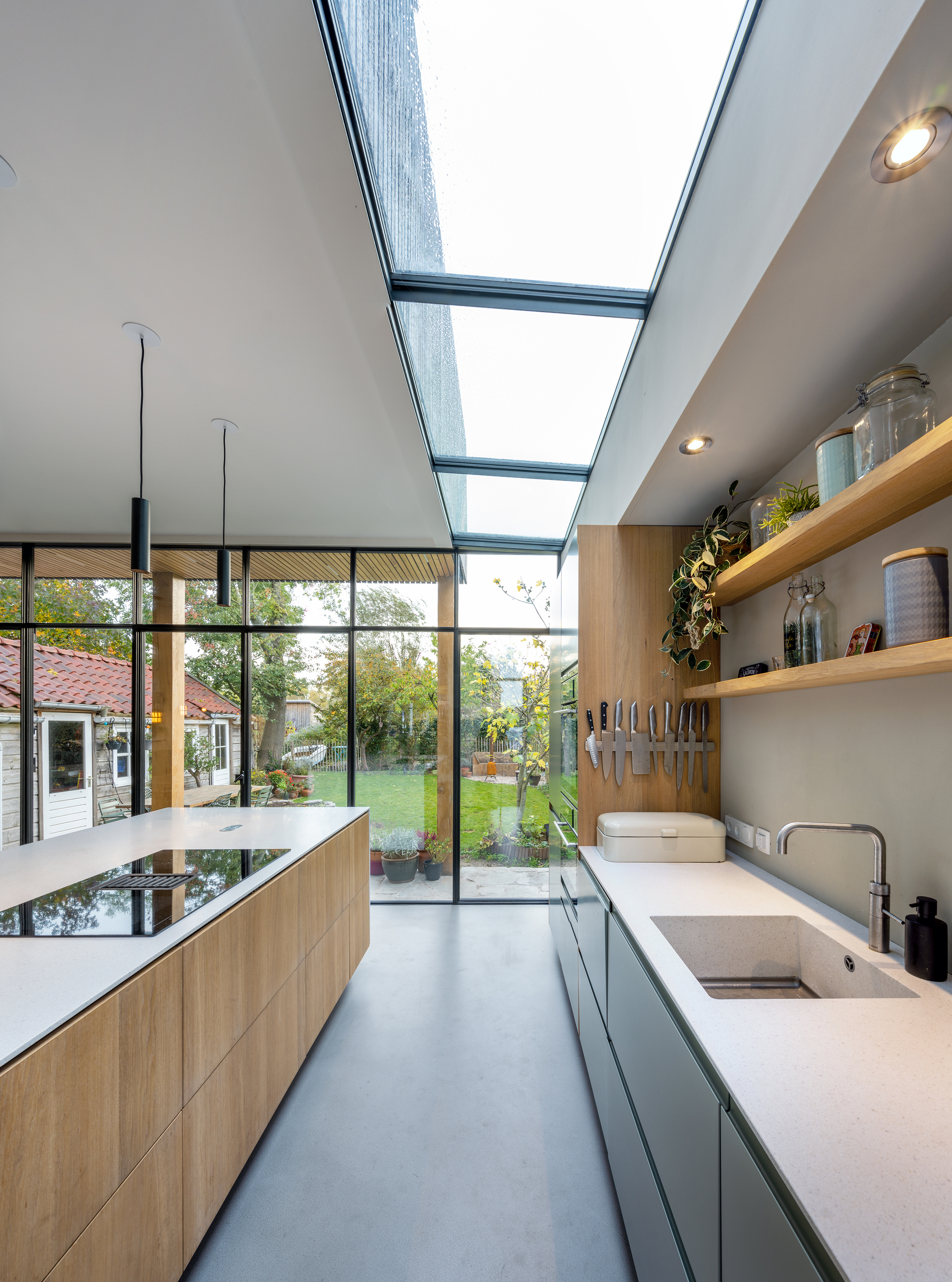Kitchen with skylight slots overhead, pale countertops, and timber shelving looking toward the planted courtyard