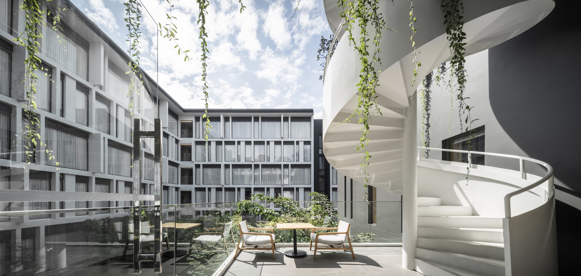 Interior courtyard with white spiral stair and cascading vines under open sky