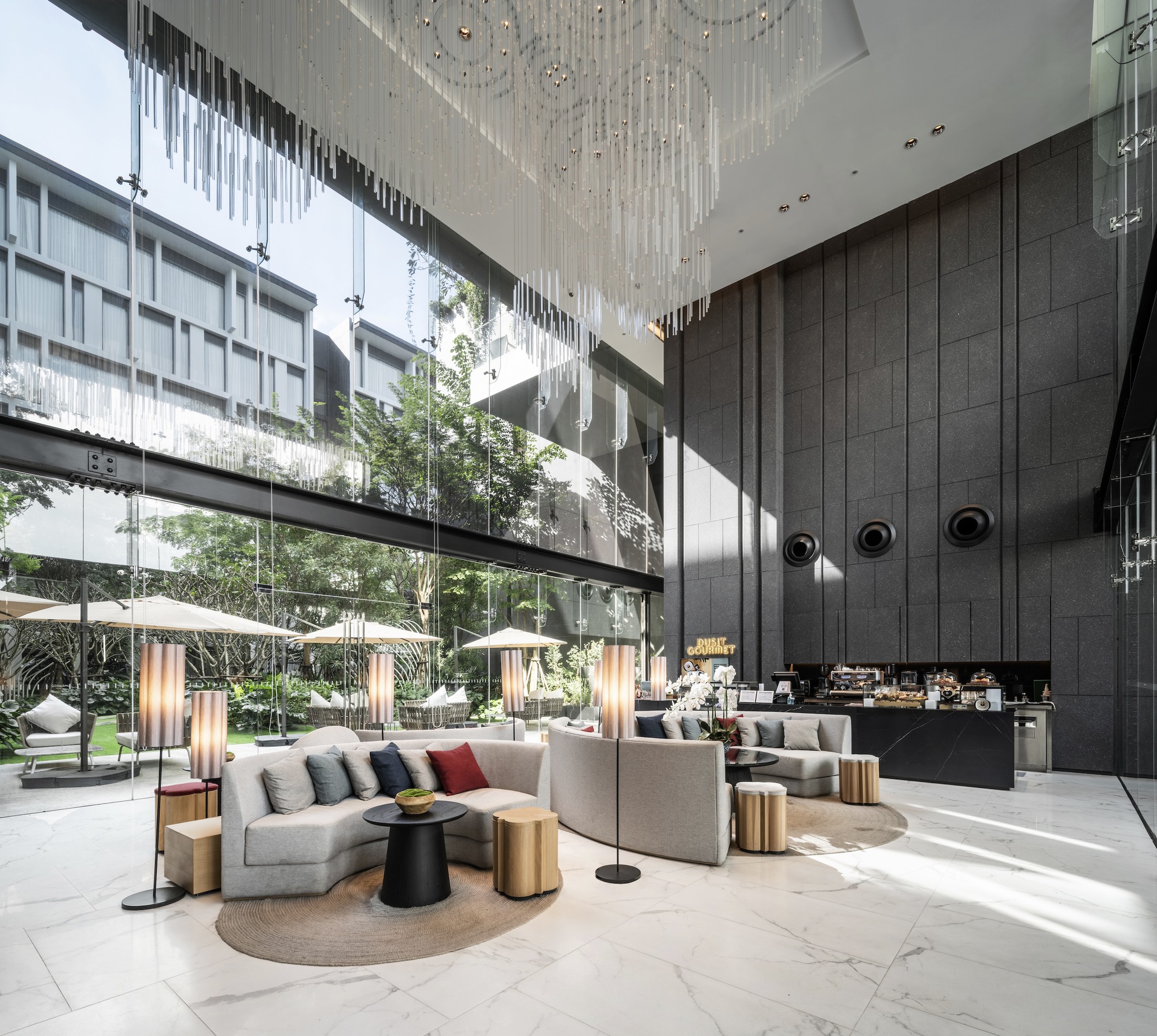 Double-height lobby with dark paneled wall and cascading crystal chandelier beside planted courtyard