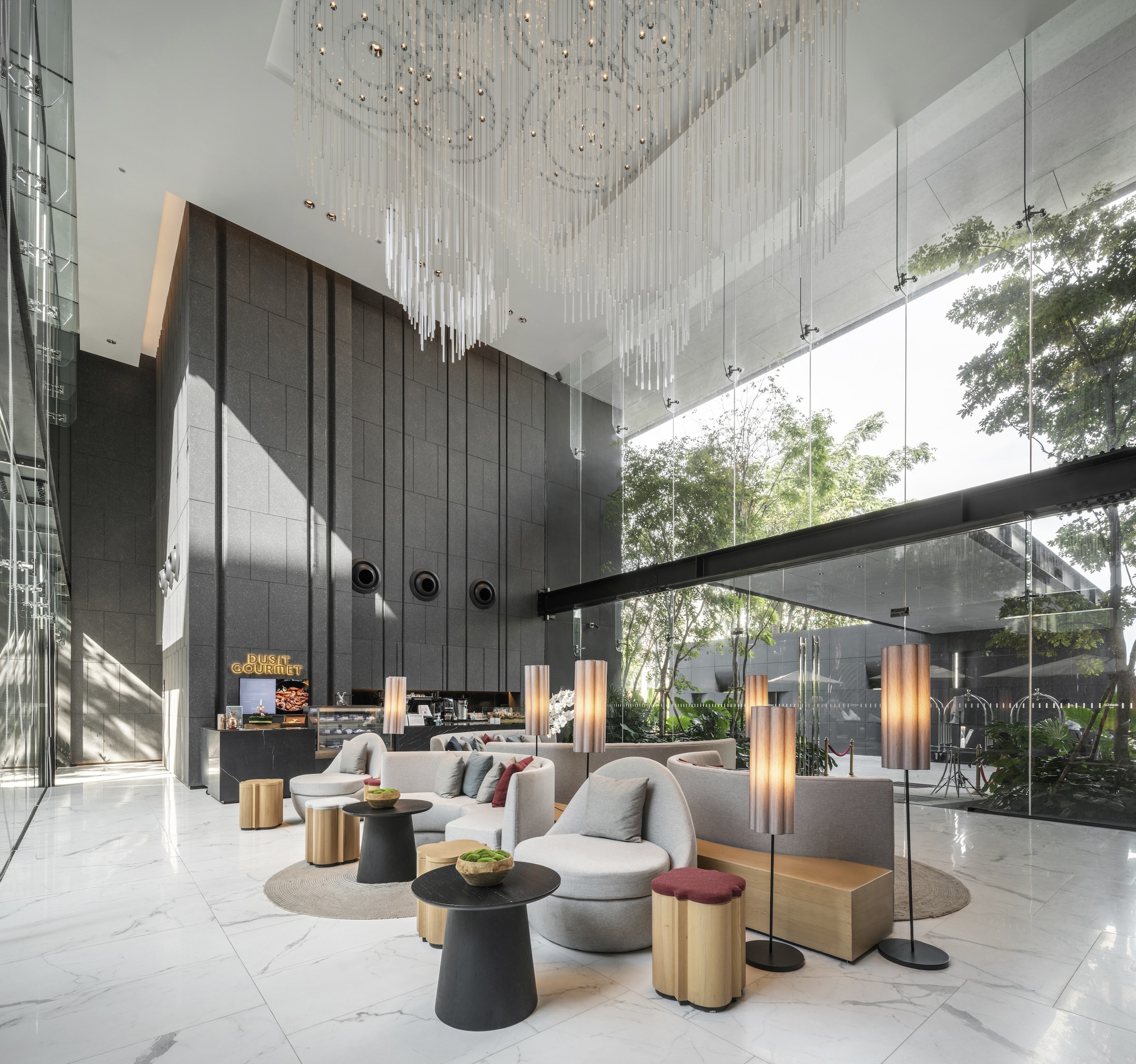 Double-height lobby with cascading crystal chandelier, dark paneled walls, and floor-to-ceiling glazing opening to a landscaped courtyard
