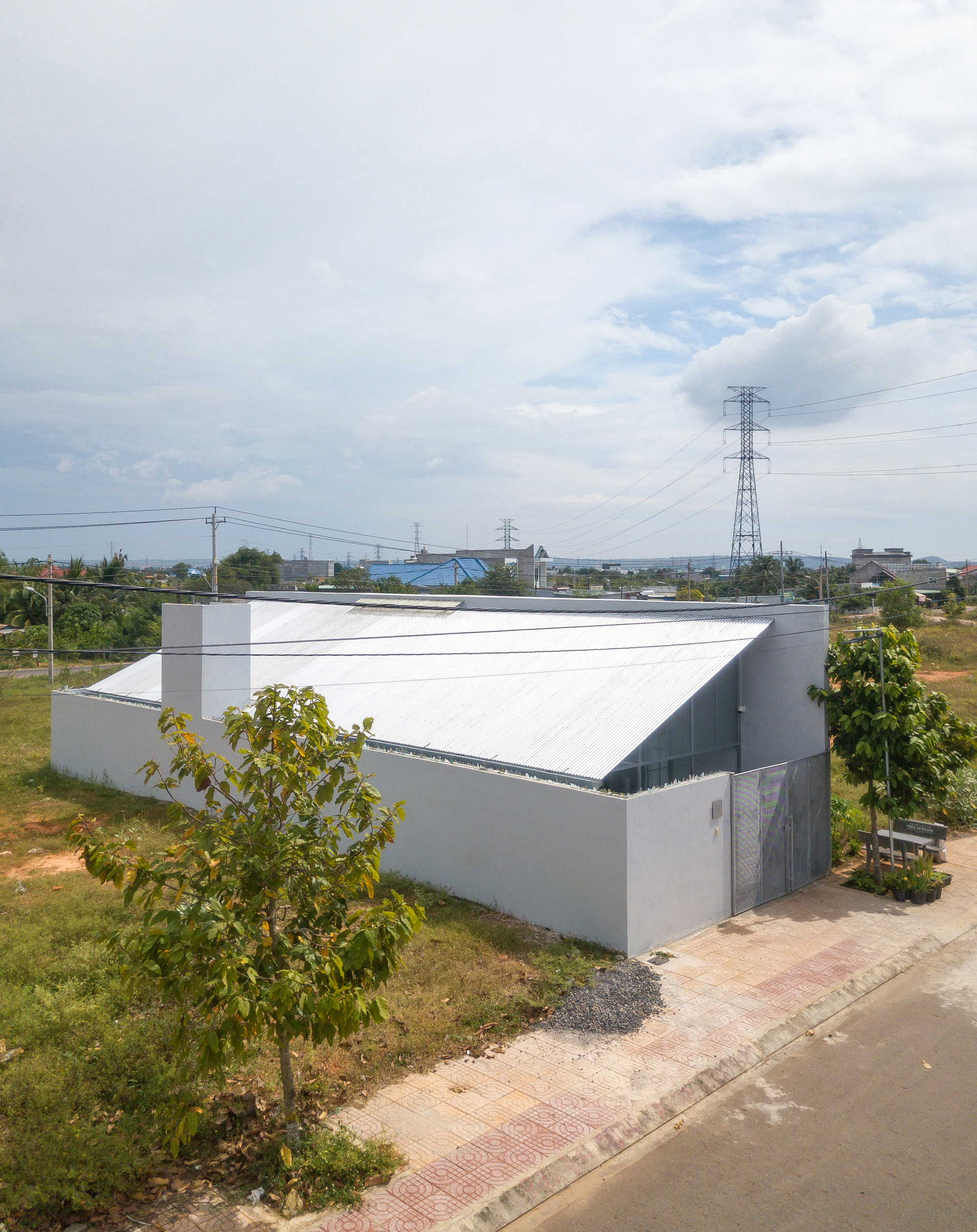 Gabled metal roof volume rising above grey masonry walls in a suburban lot with power lines overhead