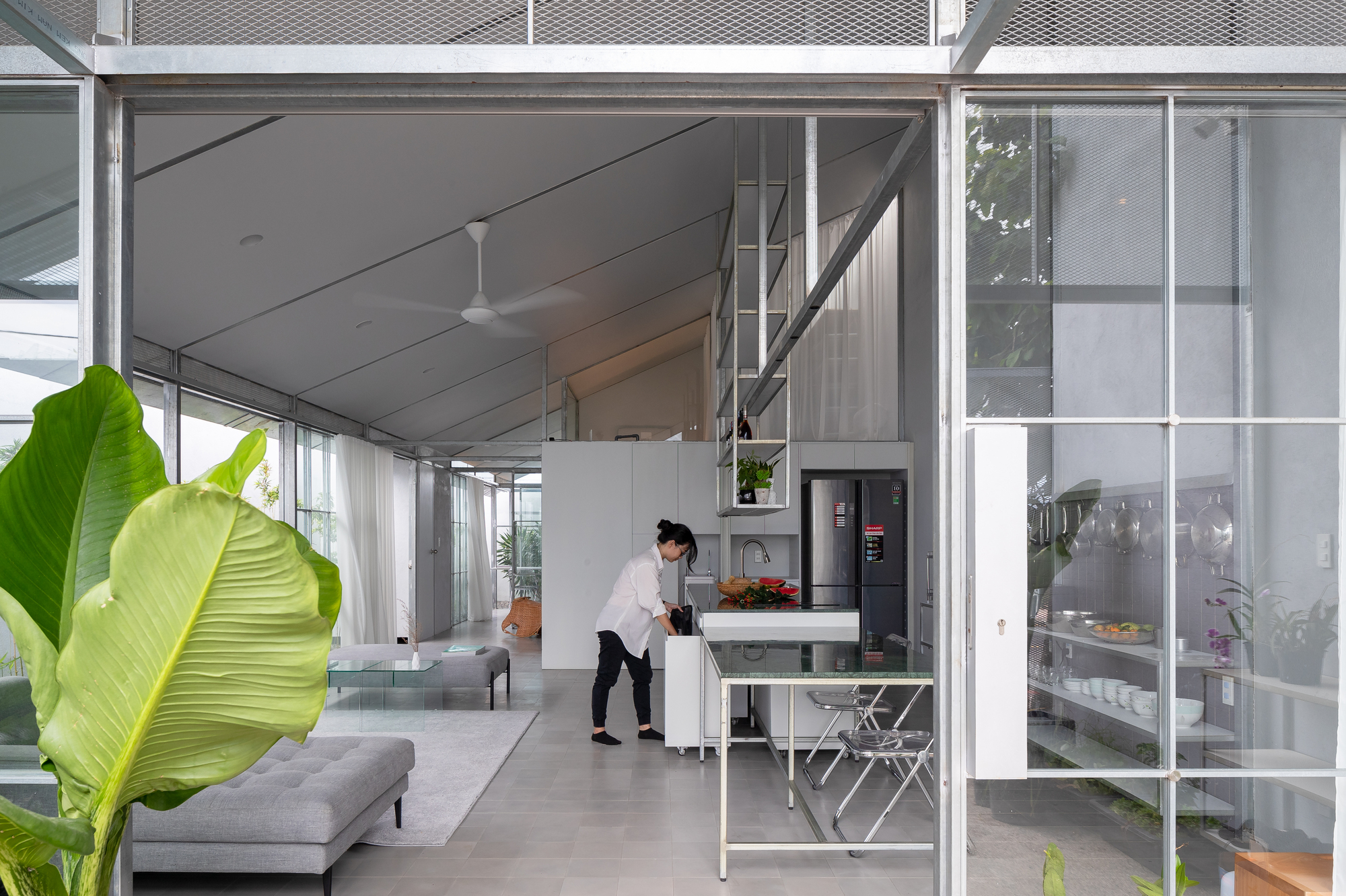 Open-plan kitchen with steel-frame partition separating living area and person preparing food at counter