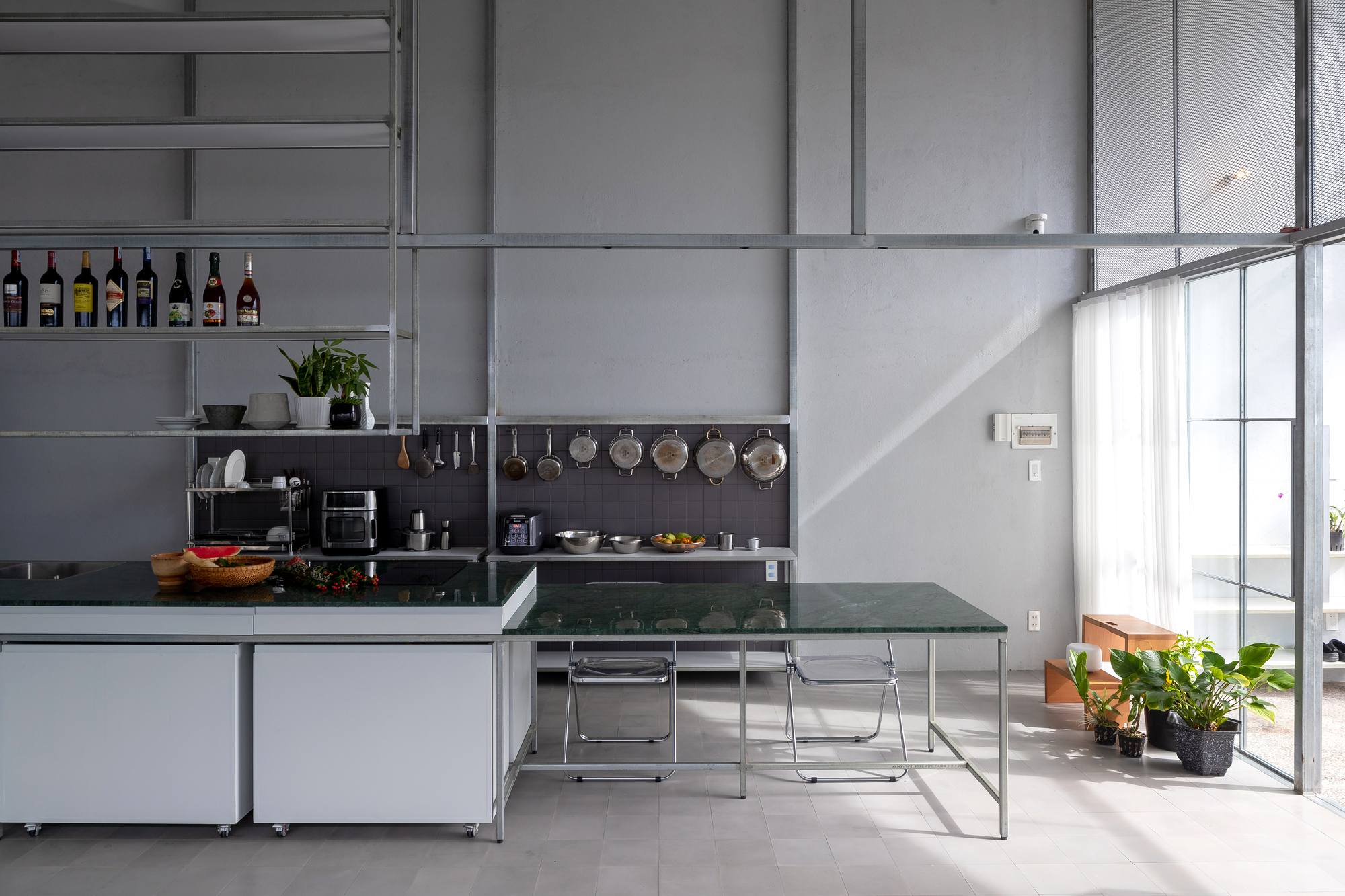 Kitchen with green glass dining table and steel shelving displaying cookware beneath afternoon sunlight
