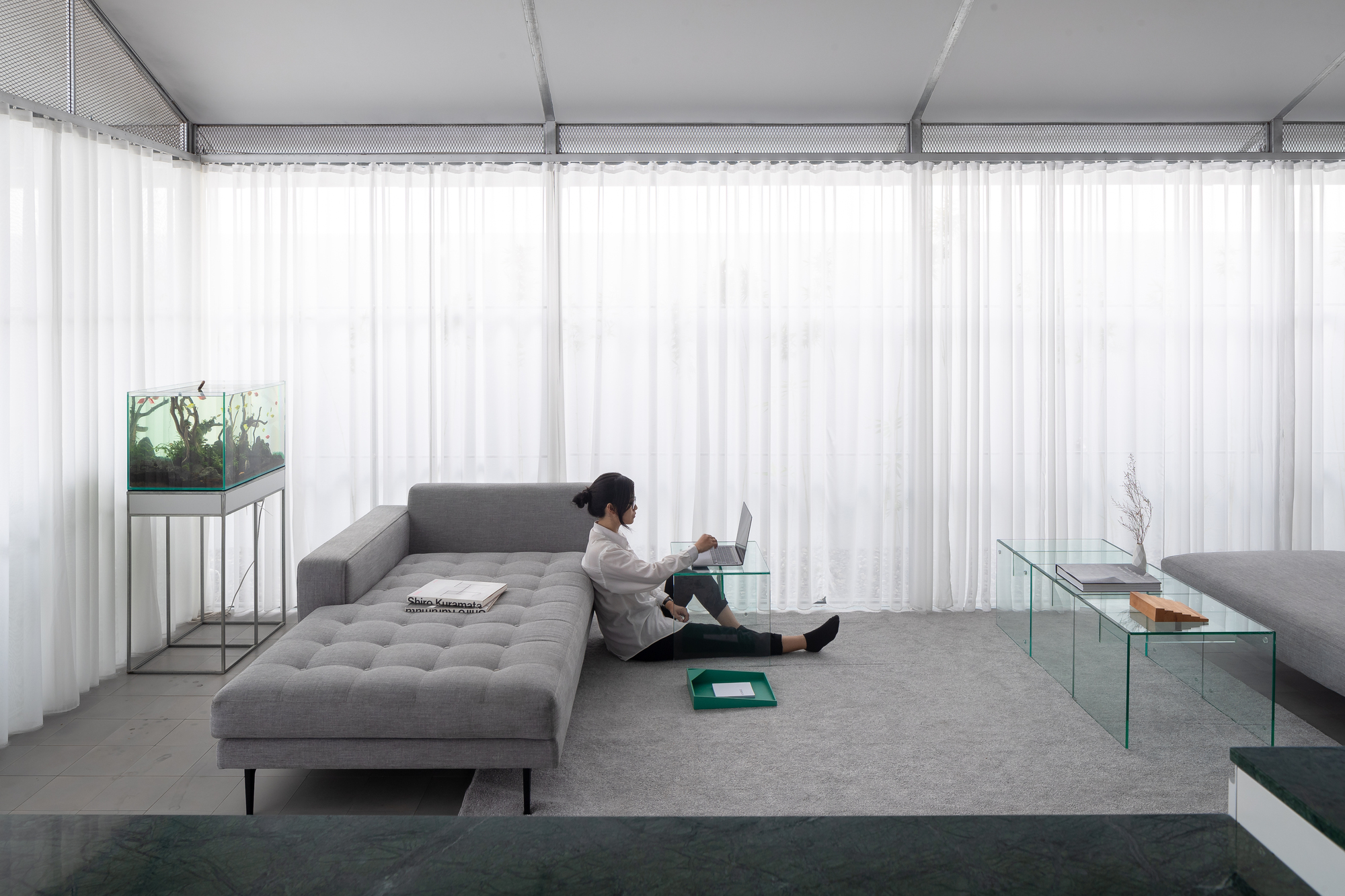 Sitting area with grey upholstered chaise and full-height white curtains filtering diffused daylight