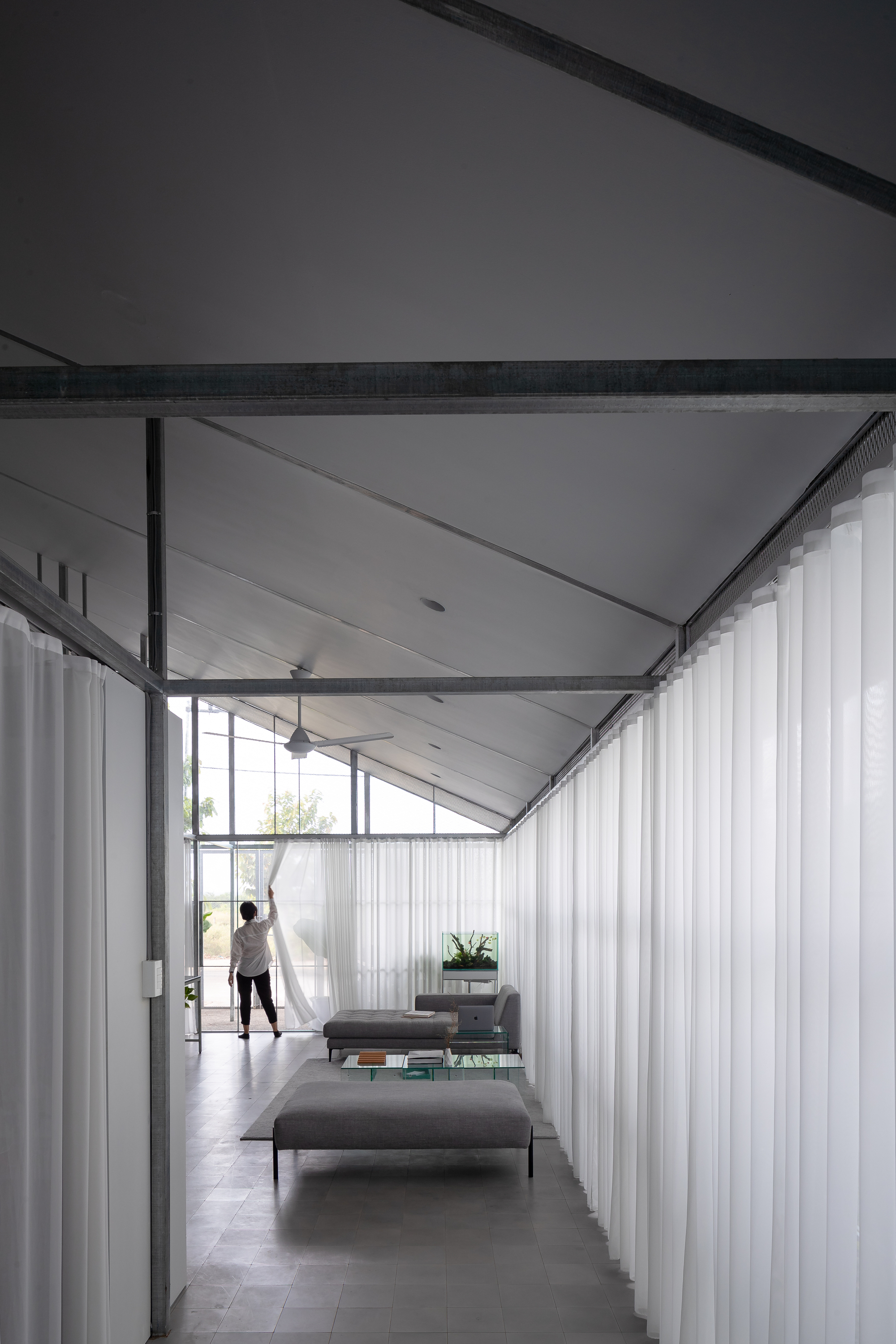 Interior corridor with exposed steel frame and white curtains flanking a figure at the window