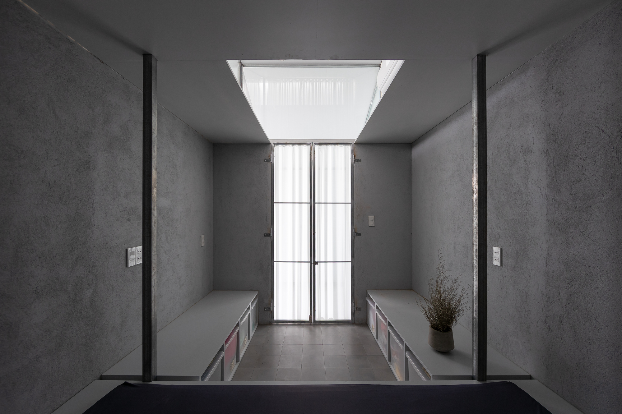 Narrow corridor framed by built-in benches with central skylight and black-tiled bathroom beyond