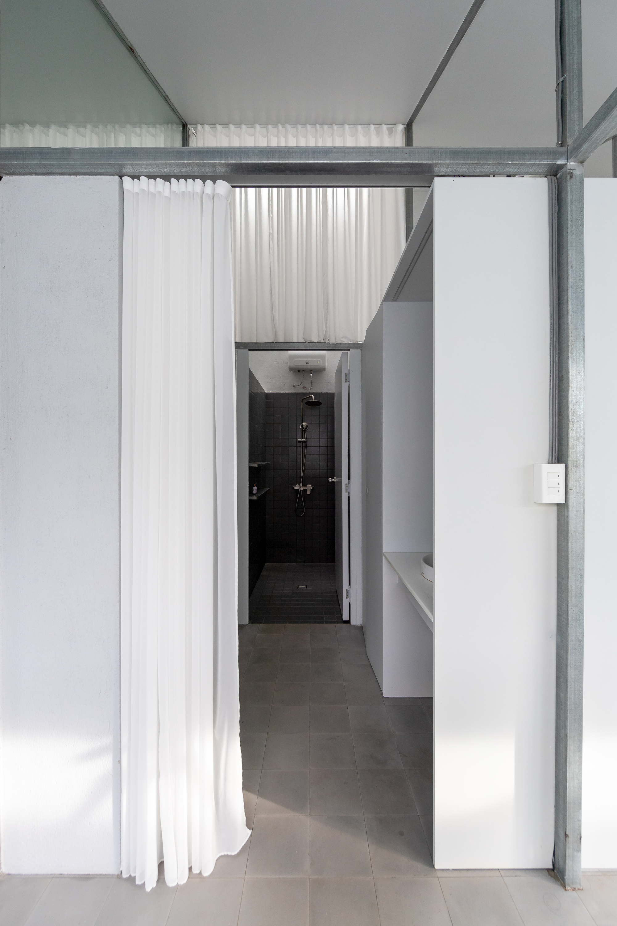 Passage with white curtain partially drawn revealing dark tiled shower enclosure under skylight