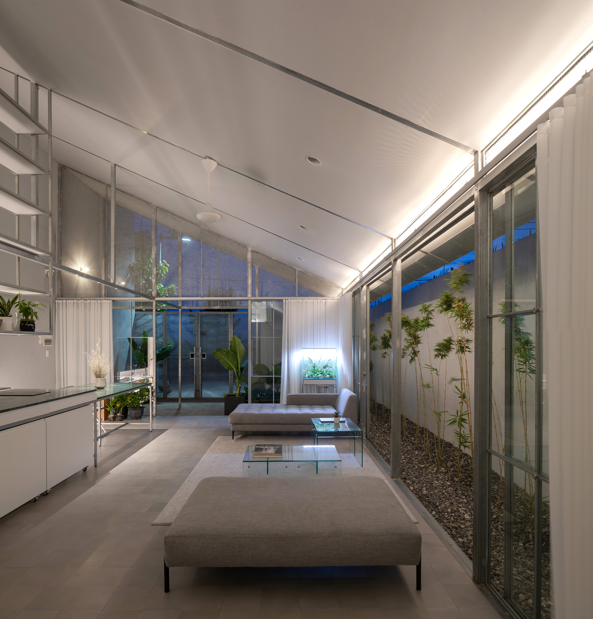 Living space with sloped ceiling and glazed walls flanking interior gravel courtyards at twilight