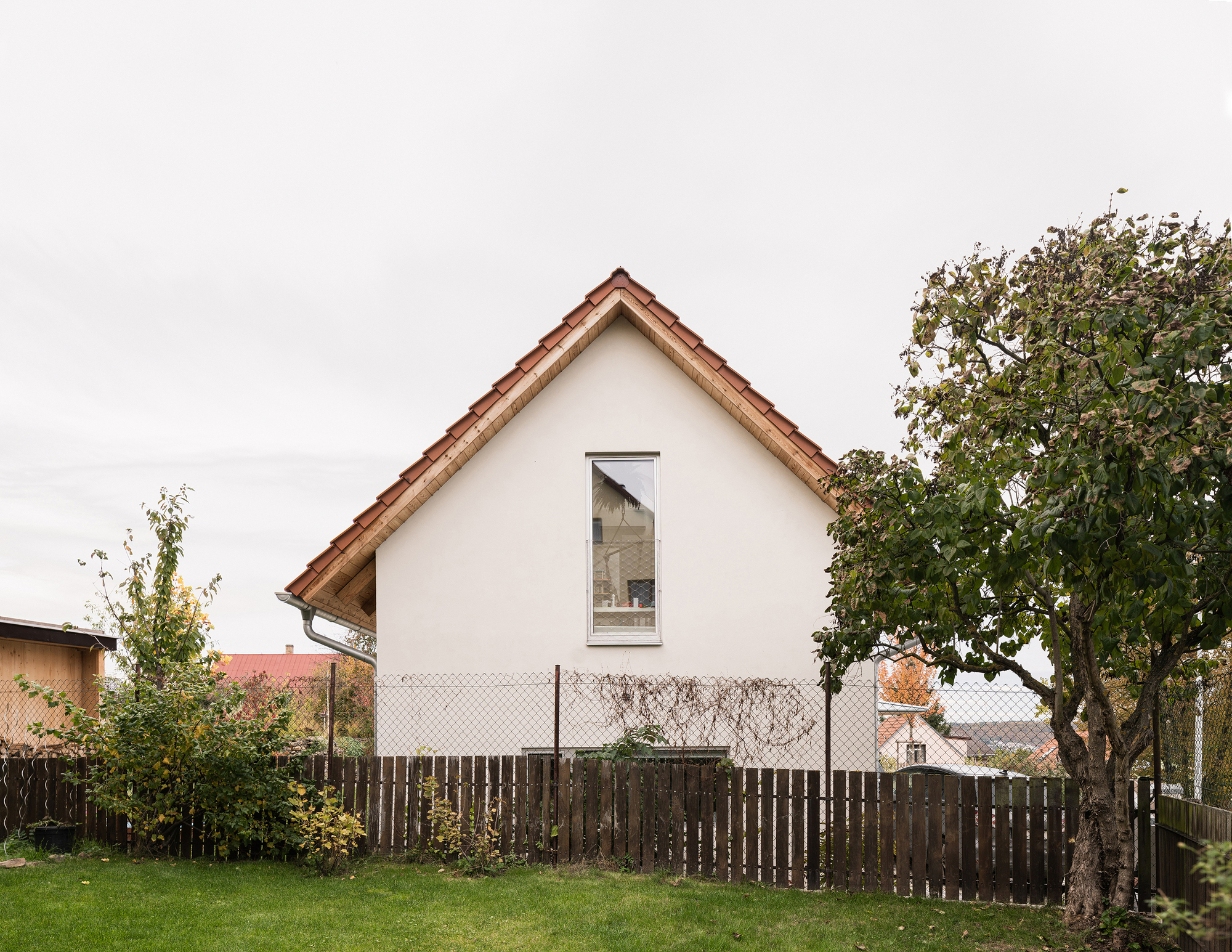 White rendered gable facade with single tall window viewed across lawn and weathered timber fence