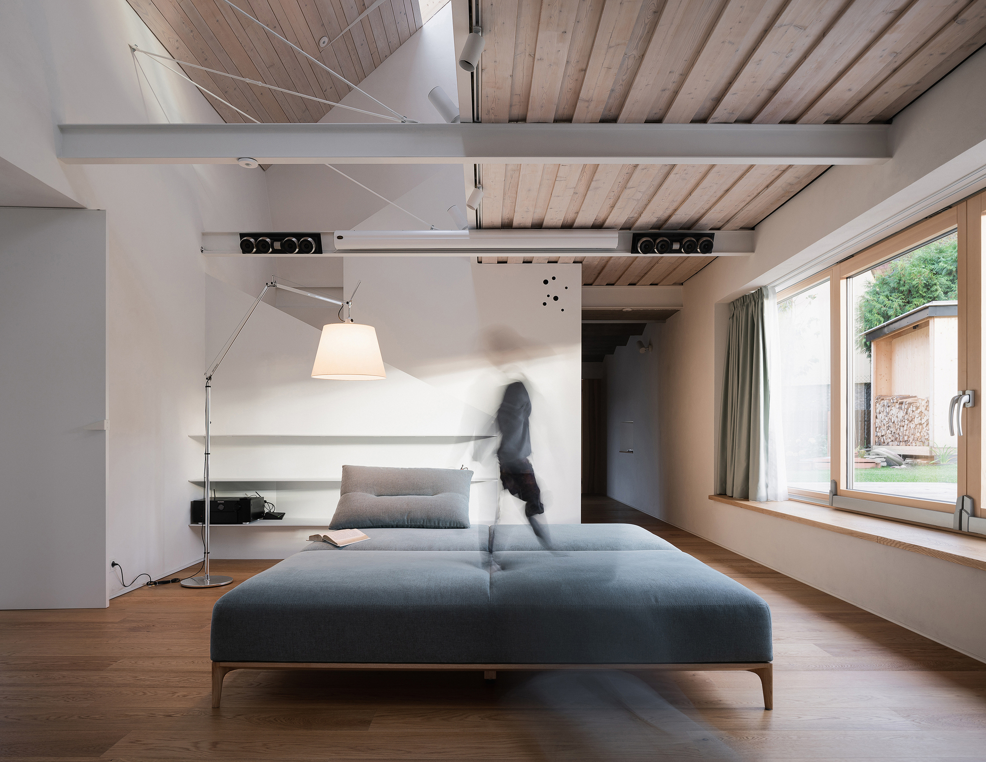 Living room with exposed timber ceiling beams and motion-blurred figure walking past daybed